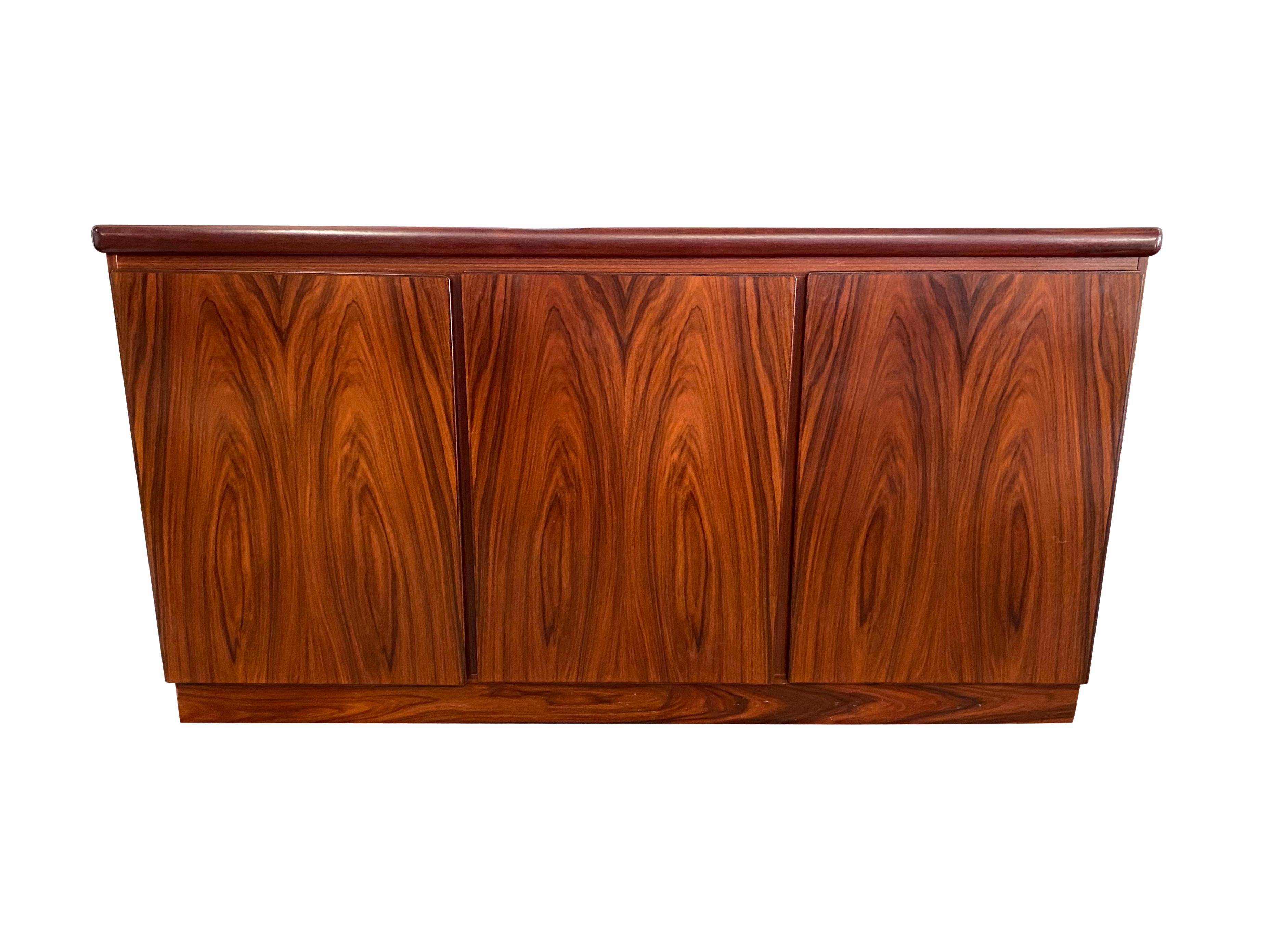 Beautiful Danish modern credenza/buffet/sideboard manufactured by Rasmus Furniture on Denmark. Simple elegant lines frame 3 ample storage compartment, one with drawers. Executed in Brazilian rosewood and featuring stunning color and grain patterns.