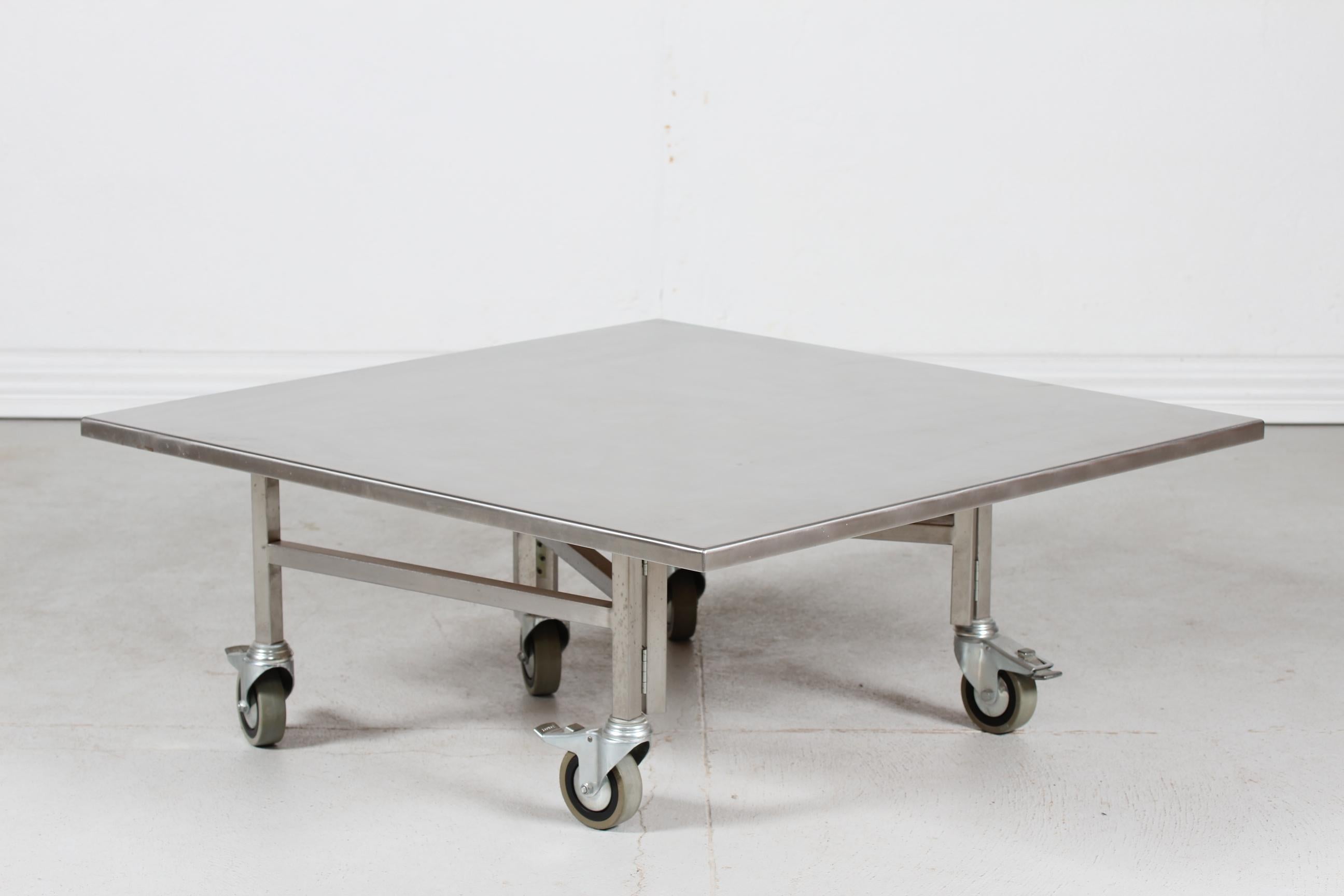 Table basse carrée danoise moderne fabriquée sur-mesure sur roulettes par un fabricant danois dans les années 1980.
La table unique est fabriquée en acier inoxydable sur le plateau, avec un cadre en métal et des roues métalliques en