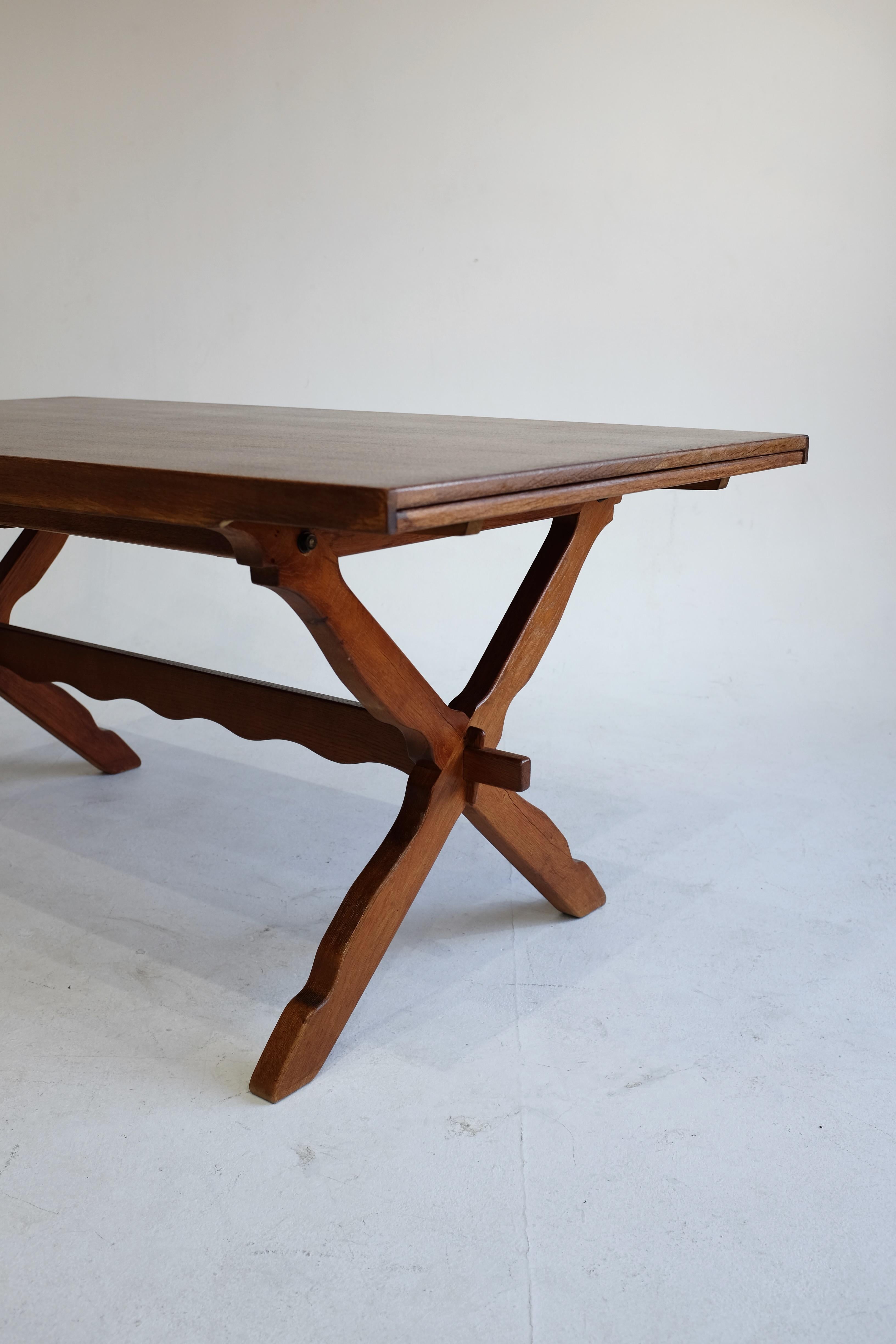Magnifique table à manger danoise moderne sculptée par Henning Kjærnulf dans un style rustique typique de ses créations. La table se compose de deux jambes croisées aux extrémités avec un design sculpté de vagues et deux extensions de feuilles pour