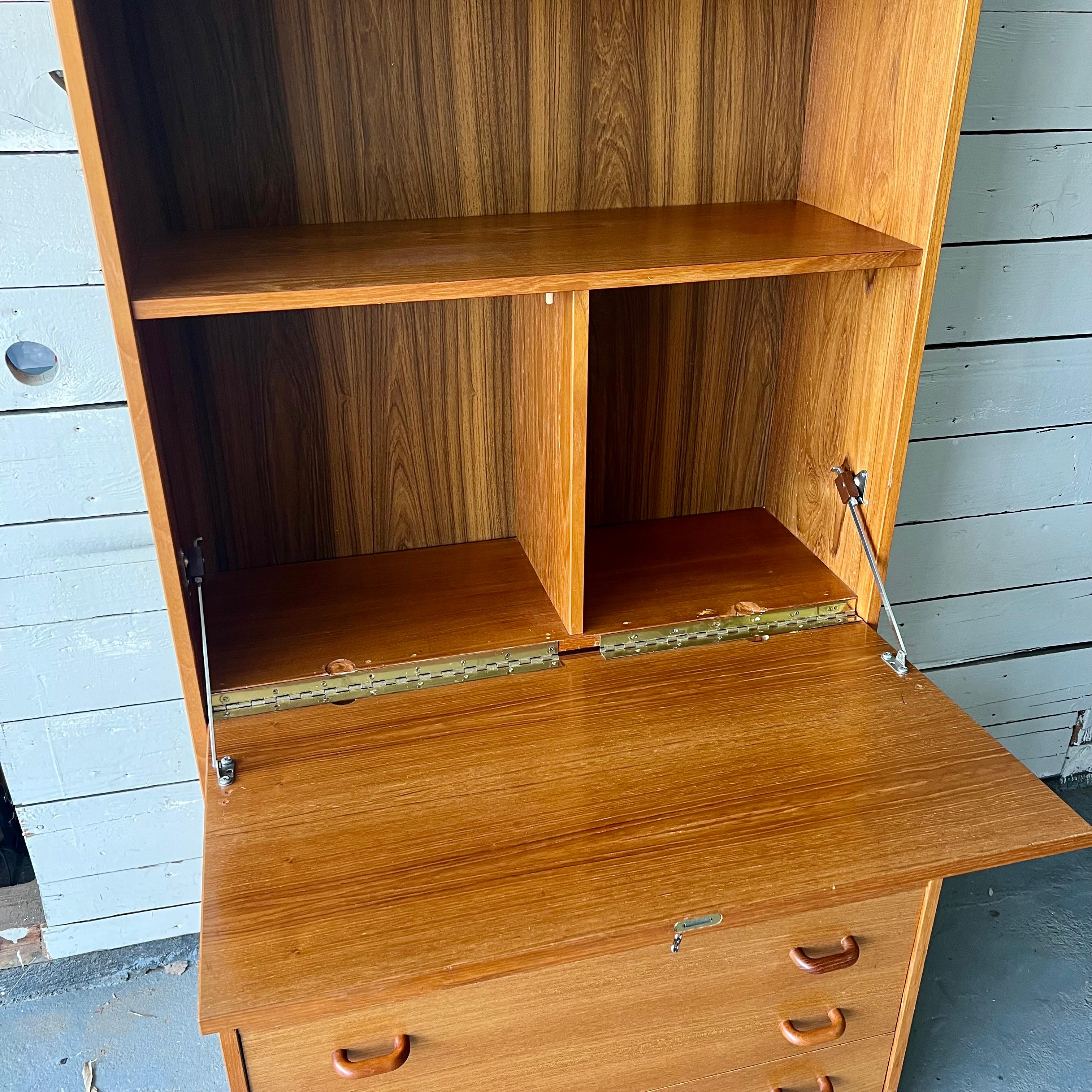 A danish modern piece by Domino Møbler. This wall unit features three storage drawers in the base with all teak pulls, a lockable drop down bar cabinet and an adjustable upper shelf. The original bar hinges had been replaced by previous owner- the