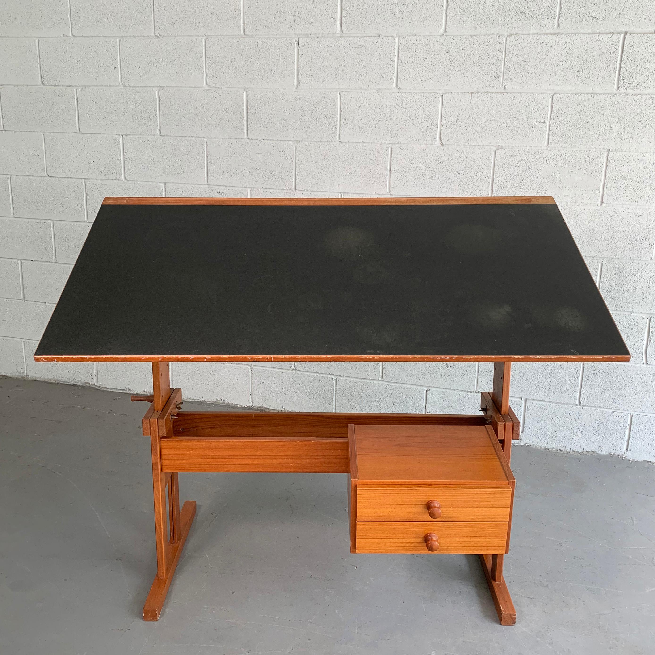 Danish modern, height and tilt adjustable, teak drafting table by Mobelfabriken Trekanten features a vinyl top and 2-drawer detachable cabinet. The top is height adjustable from 25-41 inches and tilts to 40 degrees. The drawers on the cabinet are 15