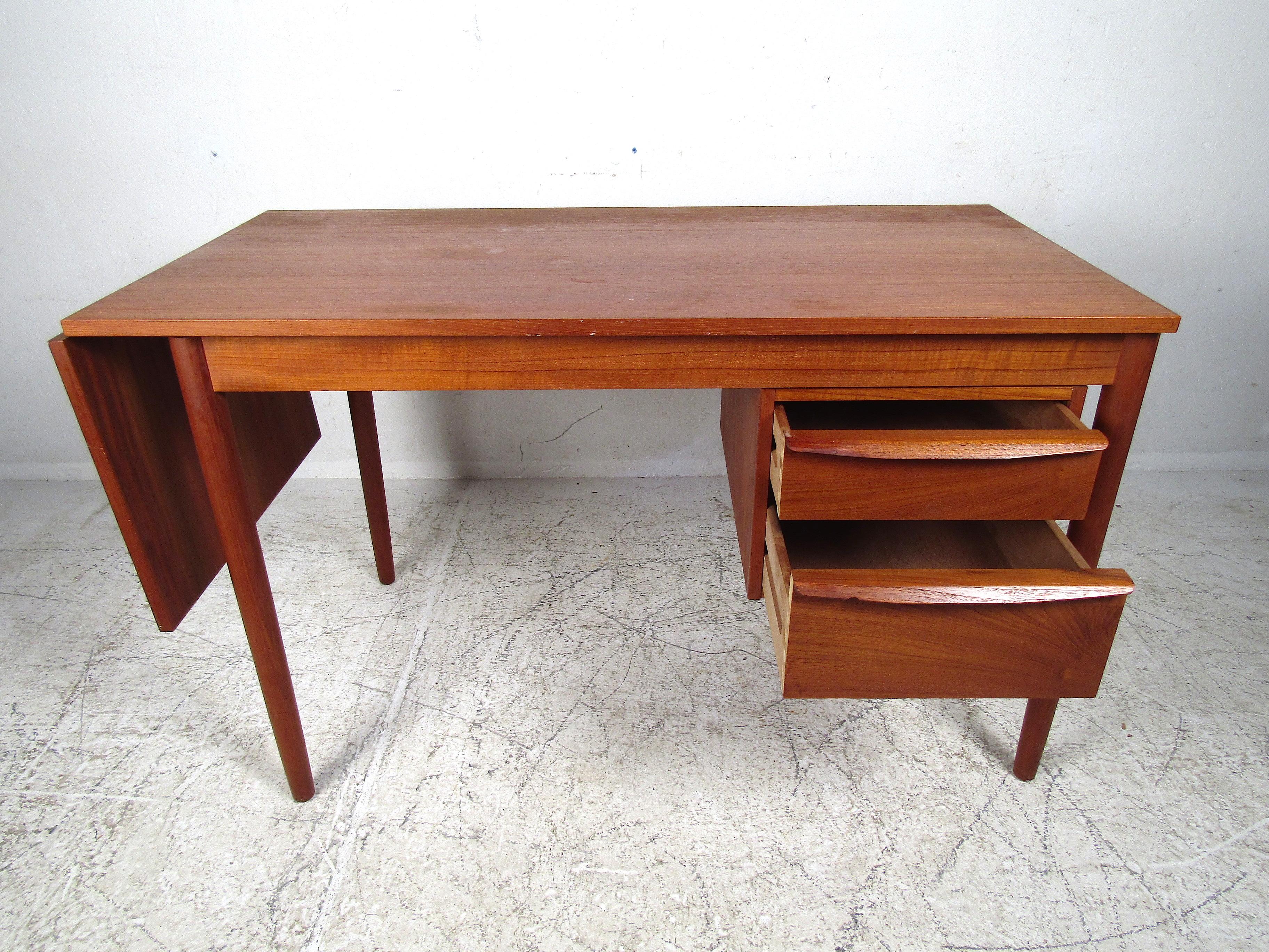 Very unusual Danish modern desk with a drop-leaf extension on the side. When extended, the entirety of the desktop slides across the base making a centered work surface. Nice teak finish throughout. Two dovetail-jointed drawers for storage. Tapered