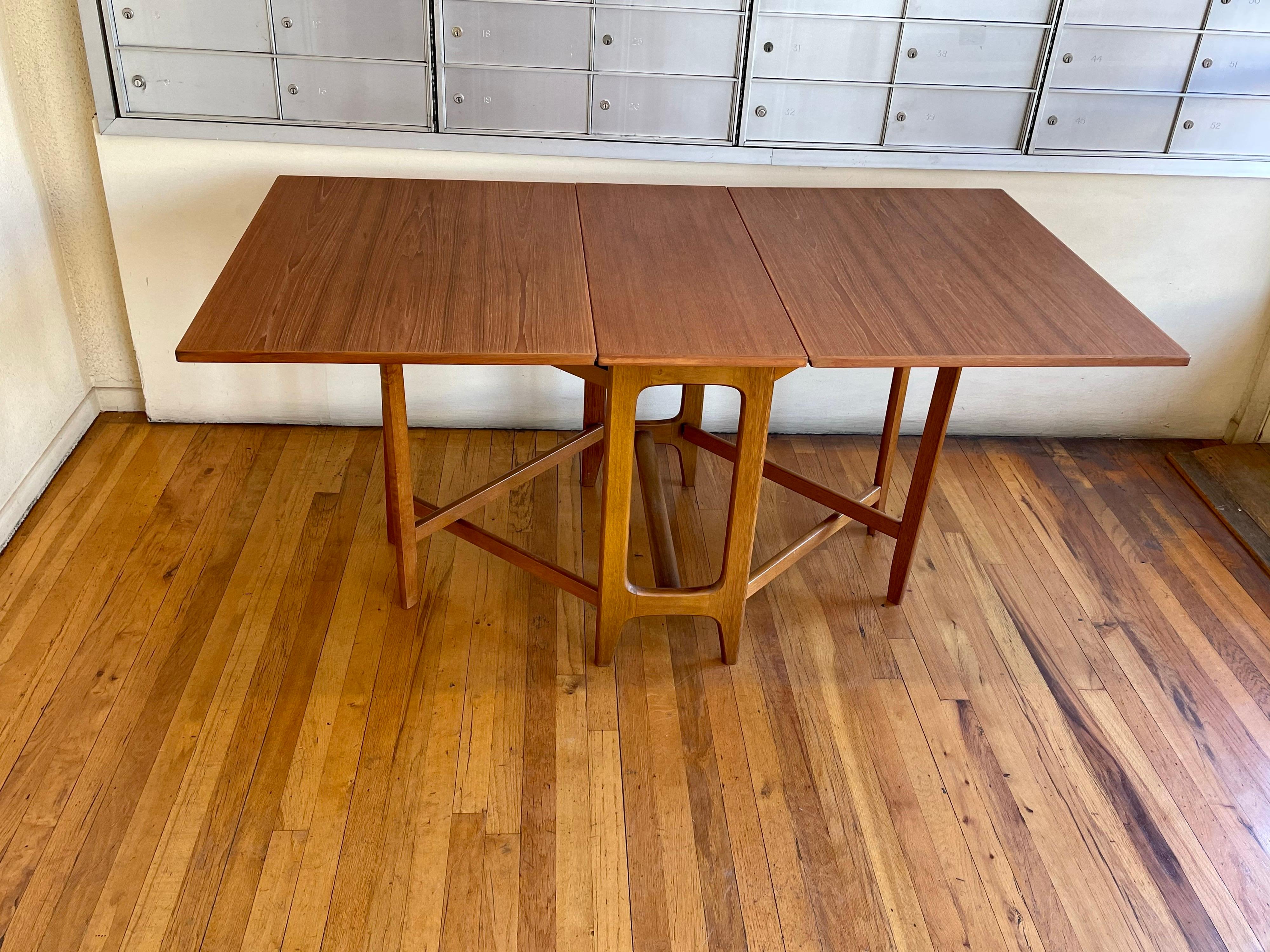 This drop-leaf dining table, teak top freshly refinished with a beechwood base, versatile and practical it can be used behind a sofa or with just one side open. The table with one leaf open its 38.5