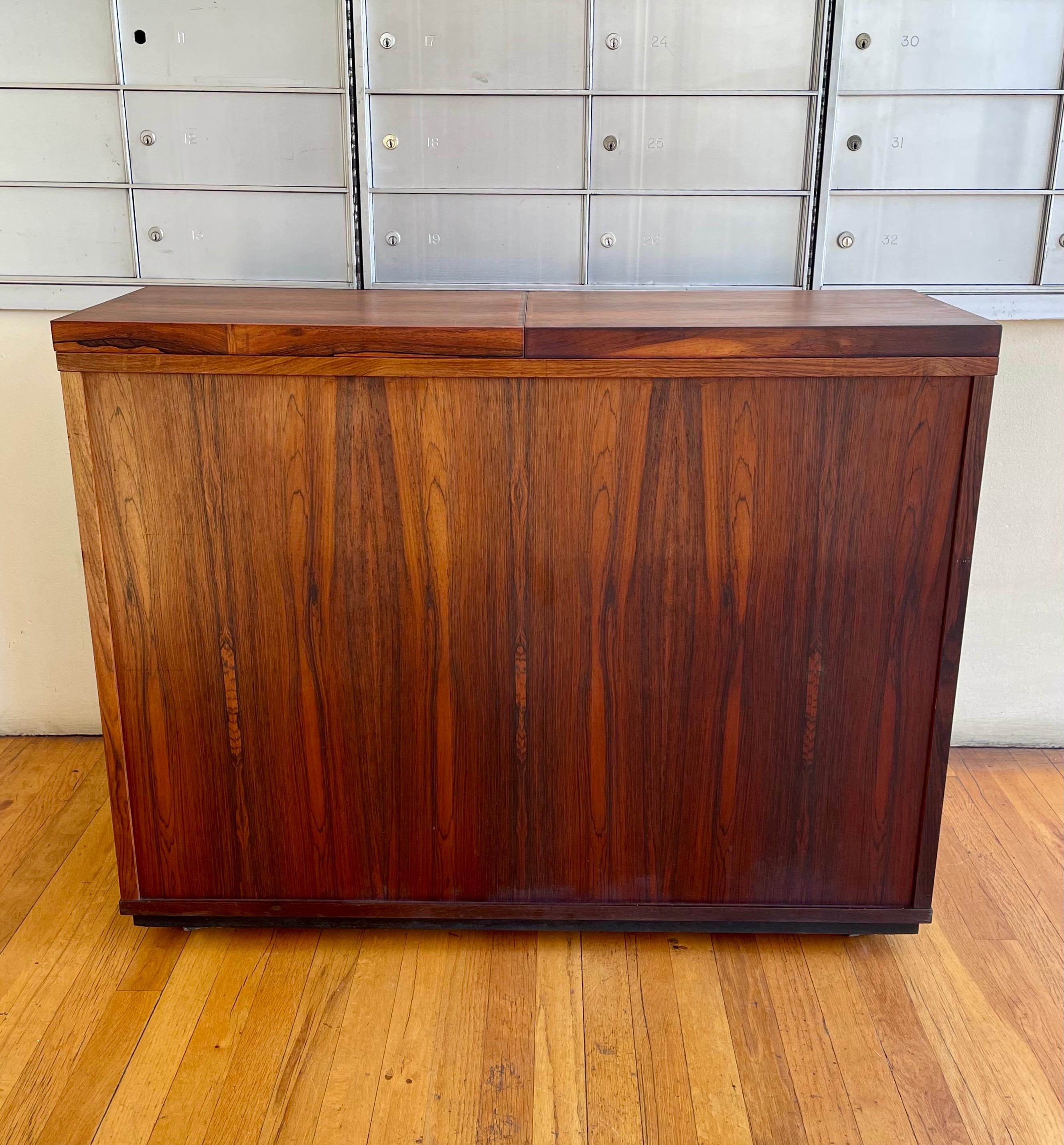 Striking beautiful versatile dry minibar cabinet designed and manufactured by Dyrlund, made in Denmark circa 1970's many compartments retractable top with white laminate under, stainless bowl and removable trays with a lock to secure the alchol. And