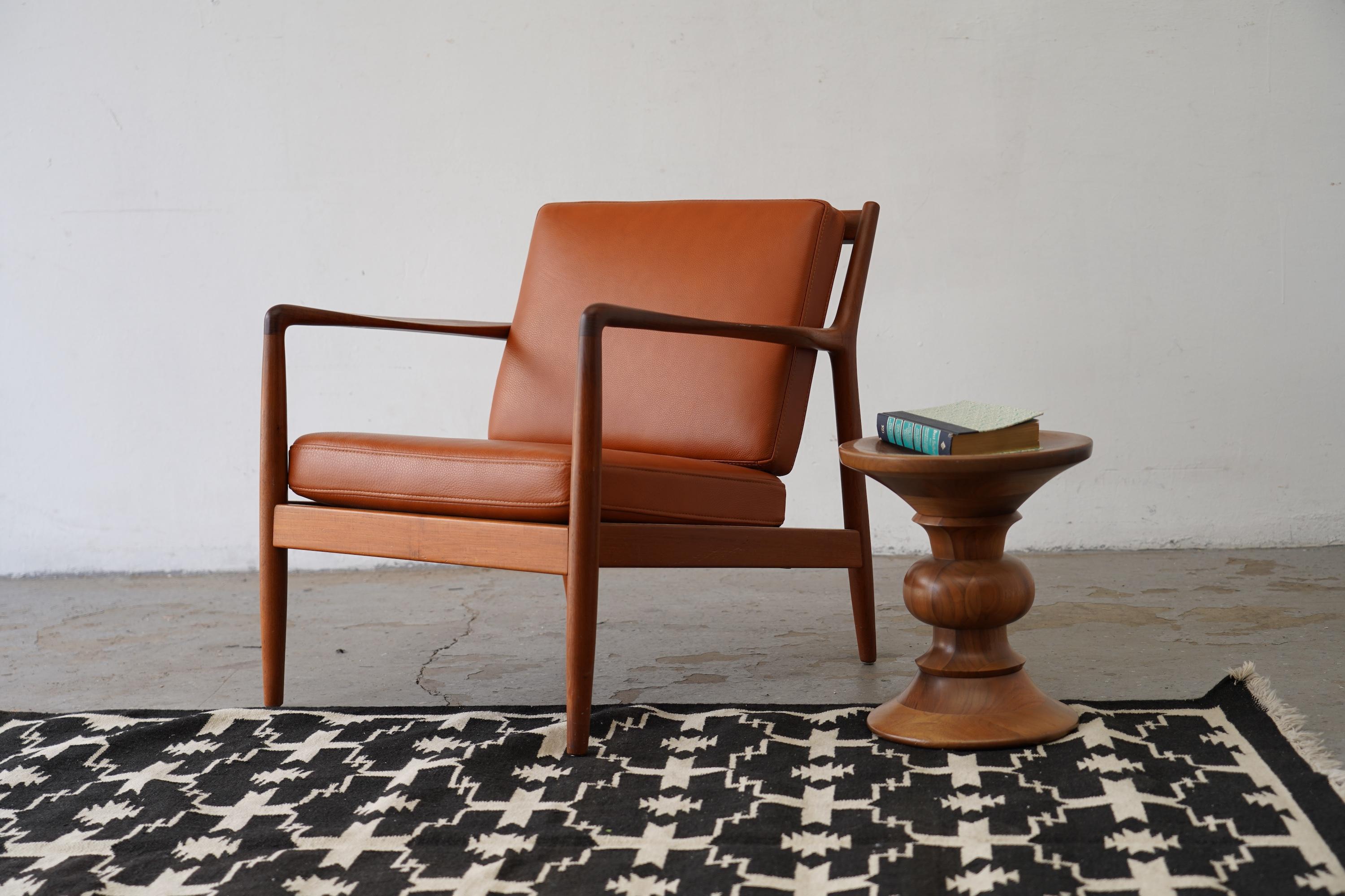 Elegant USA-75 model armchair designed by Swedish designer Folke Ohlsson for DUX. Crafted in solid teak, this iconic piece is defined by its sleek, taut armrests and gracefully angled rear legs, showcasing beautiful wood grain. The sculptural