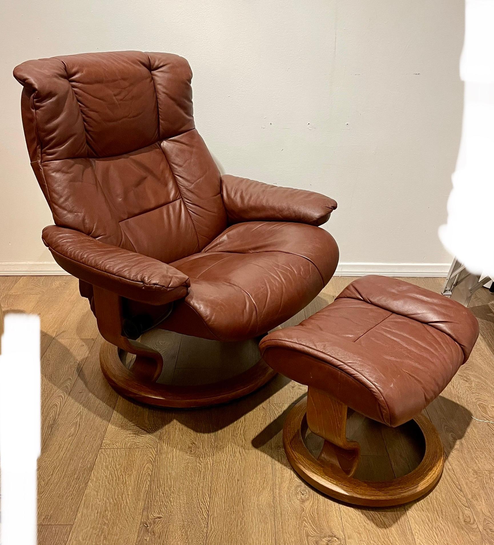 A vintage example of the modern classic reclining lounge chair and ottoman in maroon burgundy leather with a stained plywood base in walnut finish. Chair tilts and swivels. the nobs are marked with Ekornes mark.

Very good vintage and original