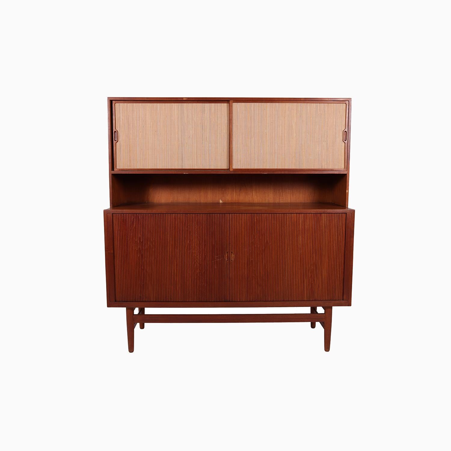 A well made sideboard designed by Erik Worts and produced by Worts Mobler. Solid teak tambour door door below with open storage and adjustable shelving. Upper half features grass cloth covered sliding doors with open storage and adjustable shelving.