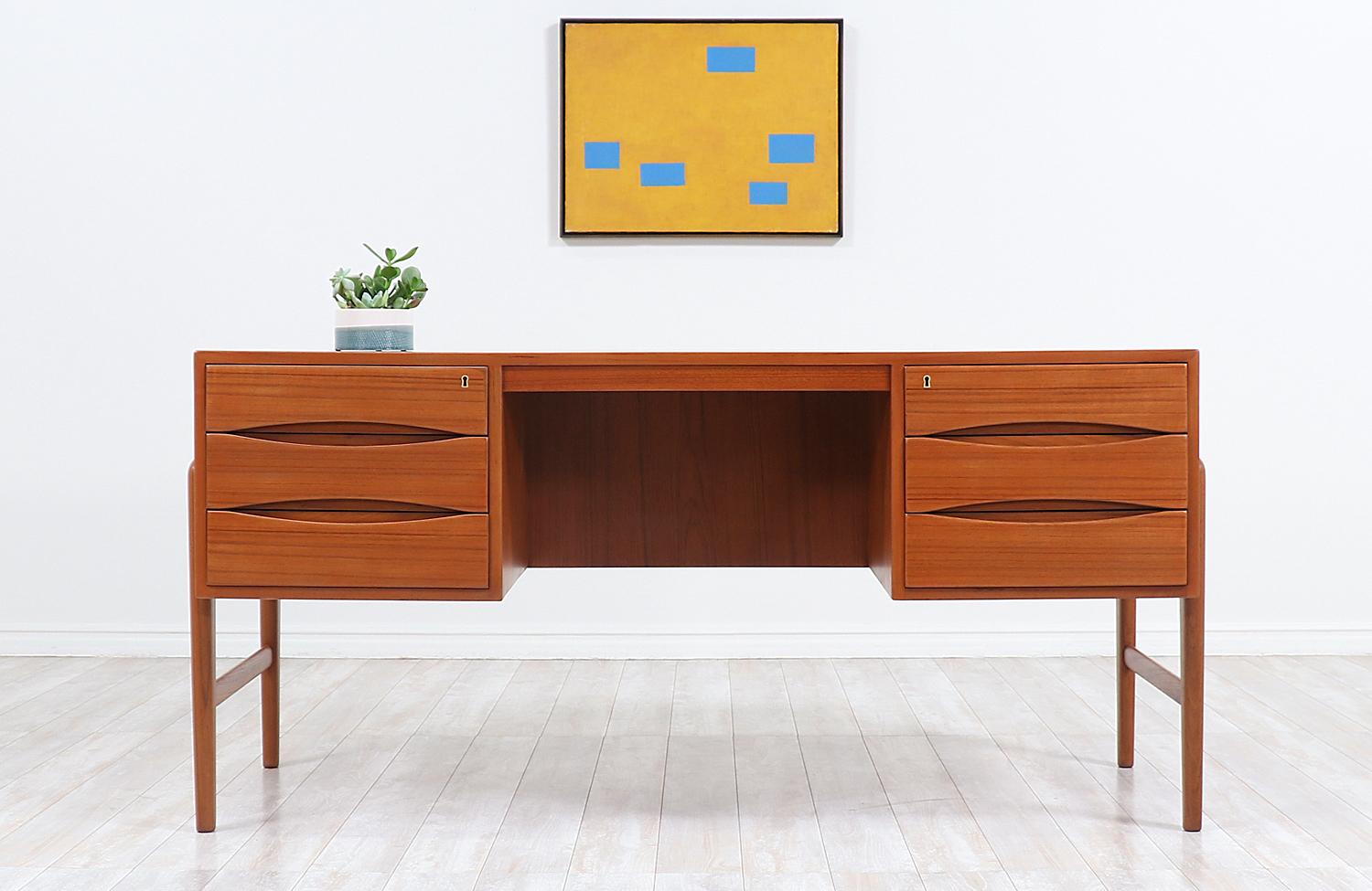 One of our most striking Danish Modern executive desks designed and made in Denmark in the 1950s. This Classic and elegant Danish desk features a solid teak frame with a stunning warm grain detail throughout and four sculpted legs that ascend from