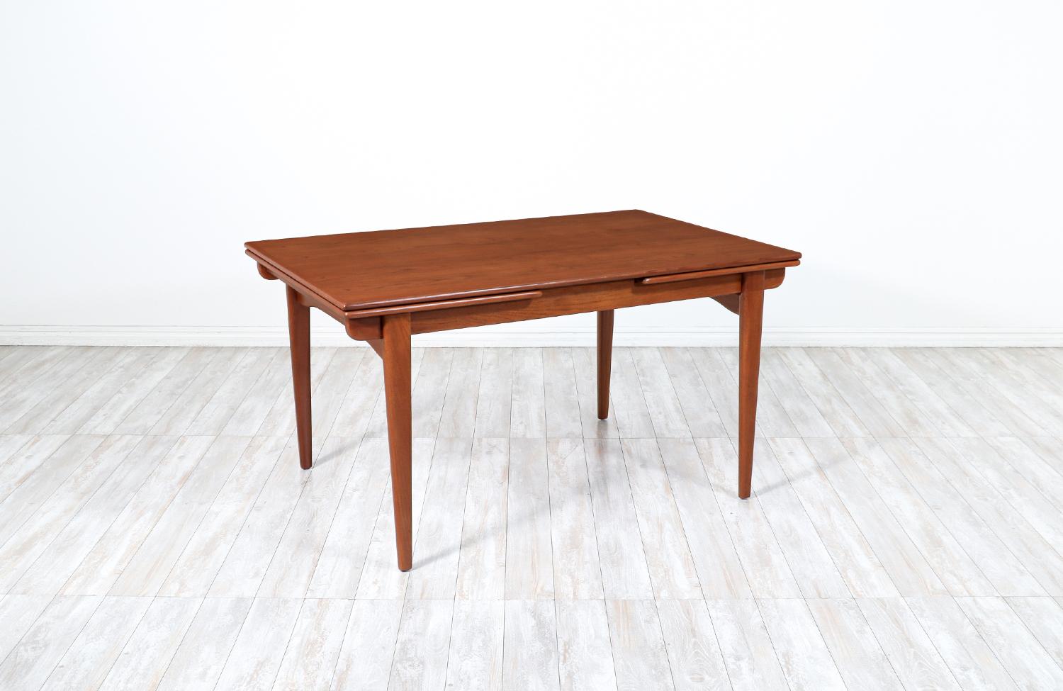 Stylish Danish Modern draw-leaf dining table by Danish furniture designer Johannes Andersen and manufactured by the workshop of Uldum Møbelfabrik, circa 1960s. This versatile table design features a solid teak wood body with a rectangular top and