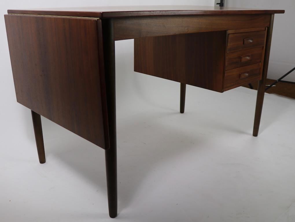 Nice Danish modern desk with three drawers, and an extendable drop side, slide top surface. Nice original condition, clean and ready to use. Top dimensions with leaf down 47.5 inch W x 63.25 inch with leaf up, or extended, position. In the style of
