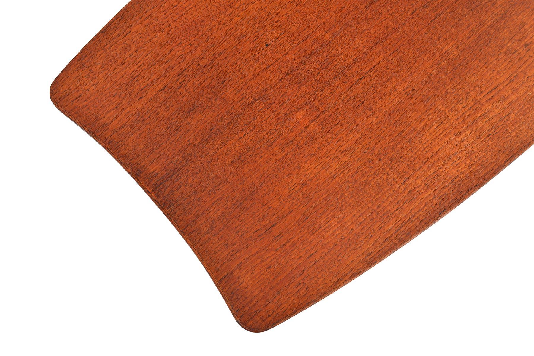This Danish modern midcentury surfboard coffee table in teak is beautifully designed. The exceptional tapering creates a dynamic Silhouette. An original cane rack offers a convenient storage solution. In excellent original condition with typical