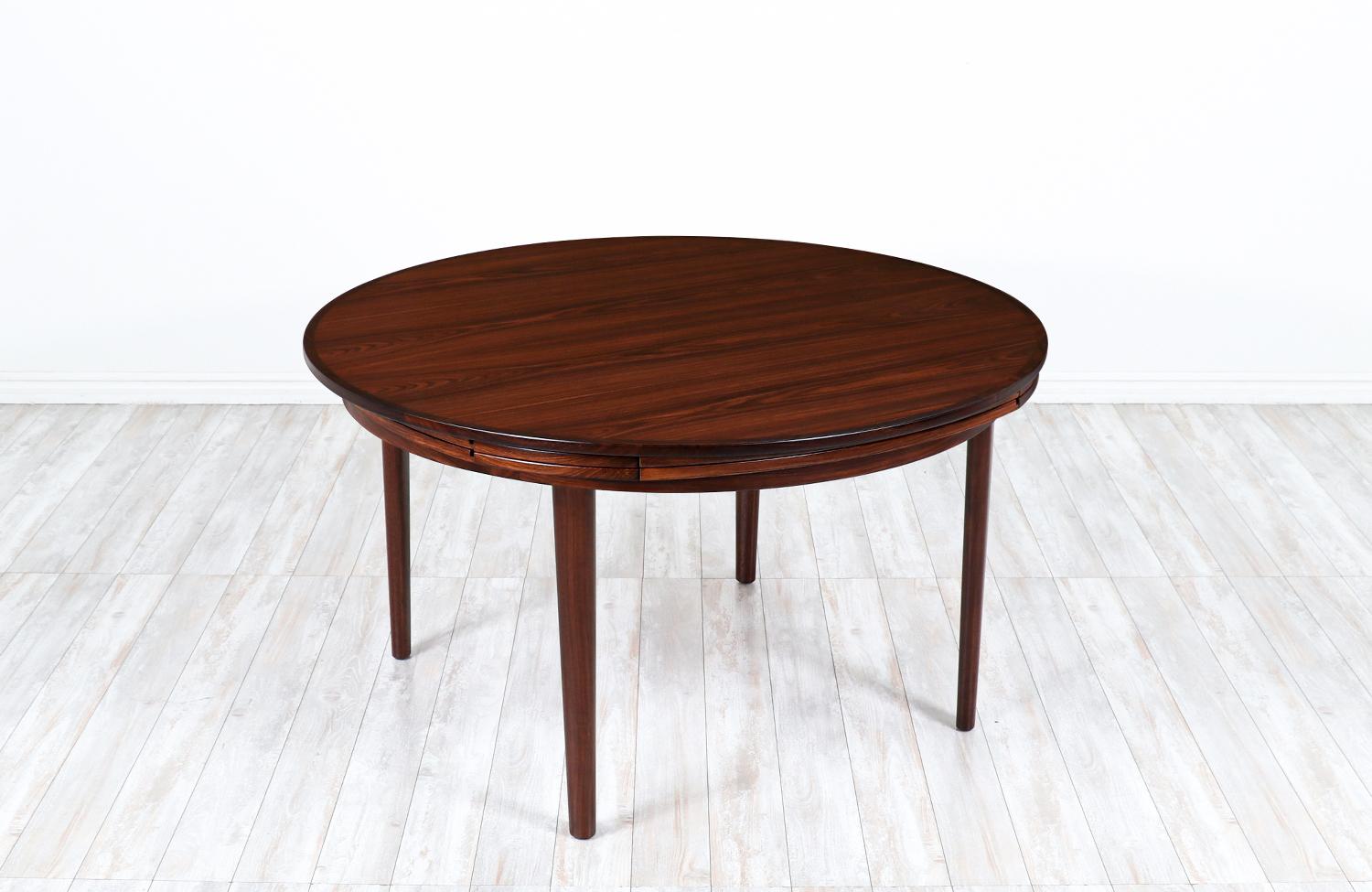 Stylish dining table designed and crafted by the famous Danish company Dyrlund in Denmark circa 1960s. This iconic table features a solid brazilian rosewood circular top with built-in extension leaves that store and draw when need to accommodate up
