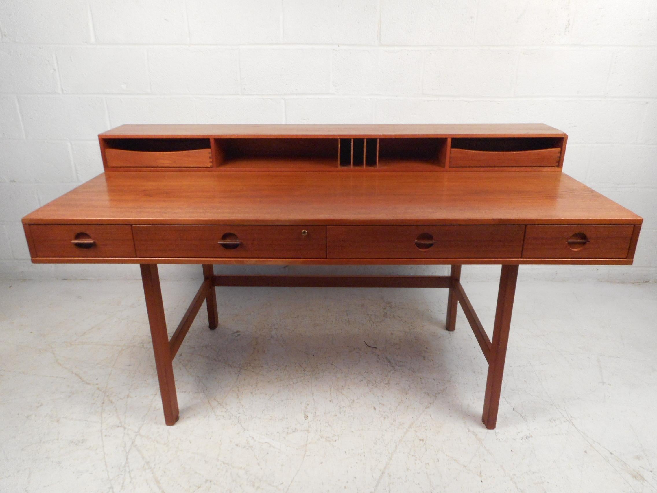 A versatile midcentury desk with plenty of room for storage and a flip top with storage trays and cubbies. This stunning Danish modern desk boasts a rich teak finish, four large drawers, and stretchers along the base for added sturdiness. When the