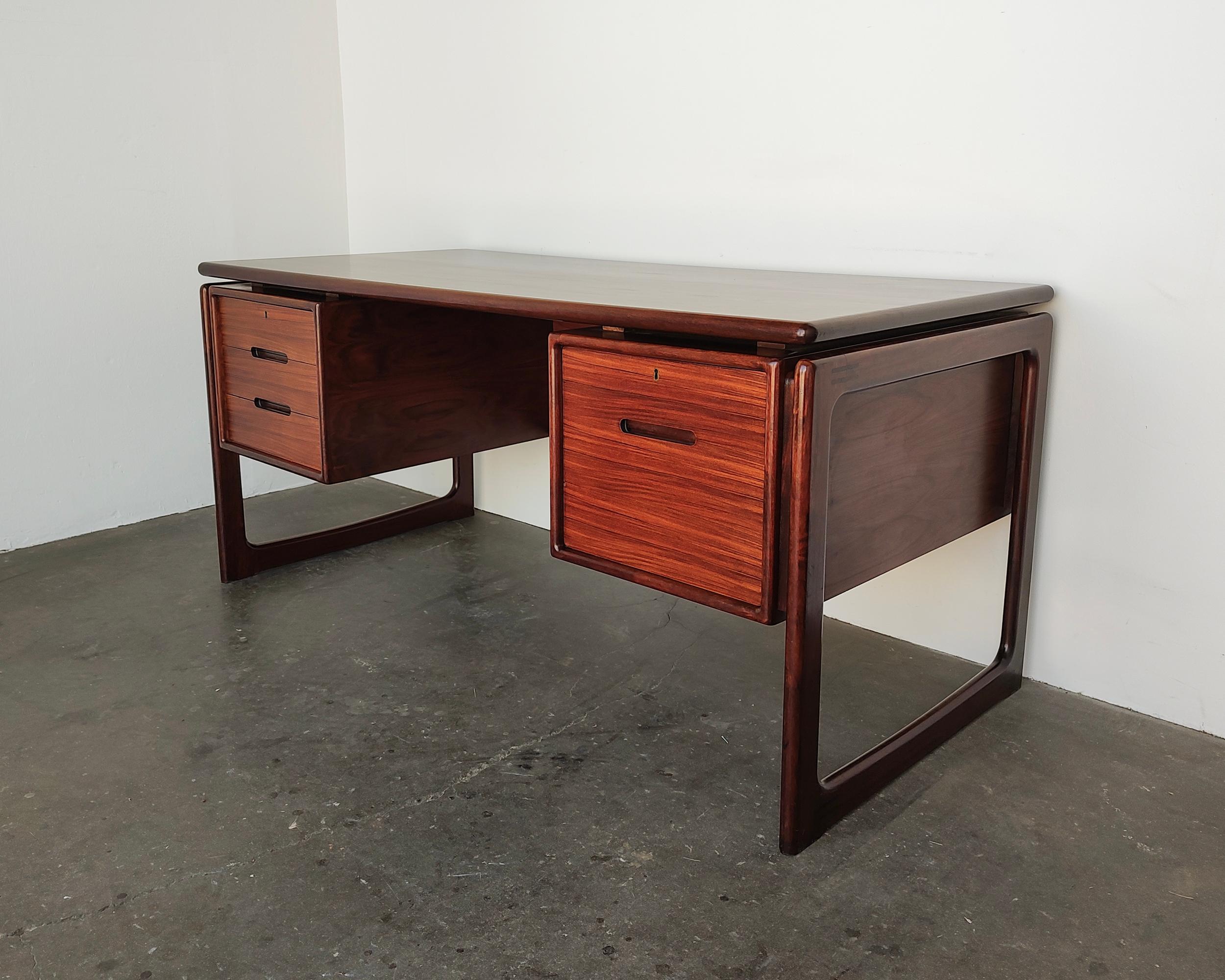 Danish mid-century rosewood desk by Dyrlund circa 1970s. Beautiful rosewood grain covering entire pieces, with solid sled legs and recessed pulls. Backside features built-in open shelf cubbies. Overall great vintage condition, some light fading on