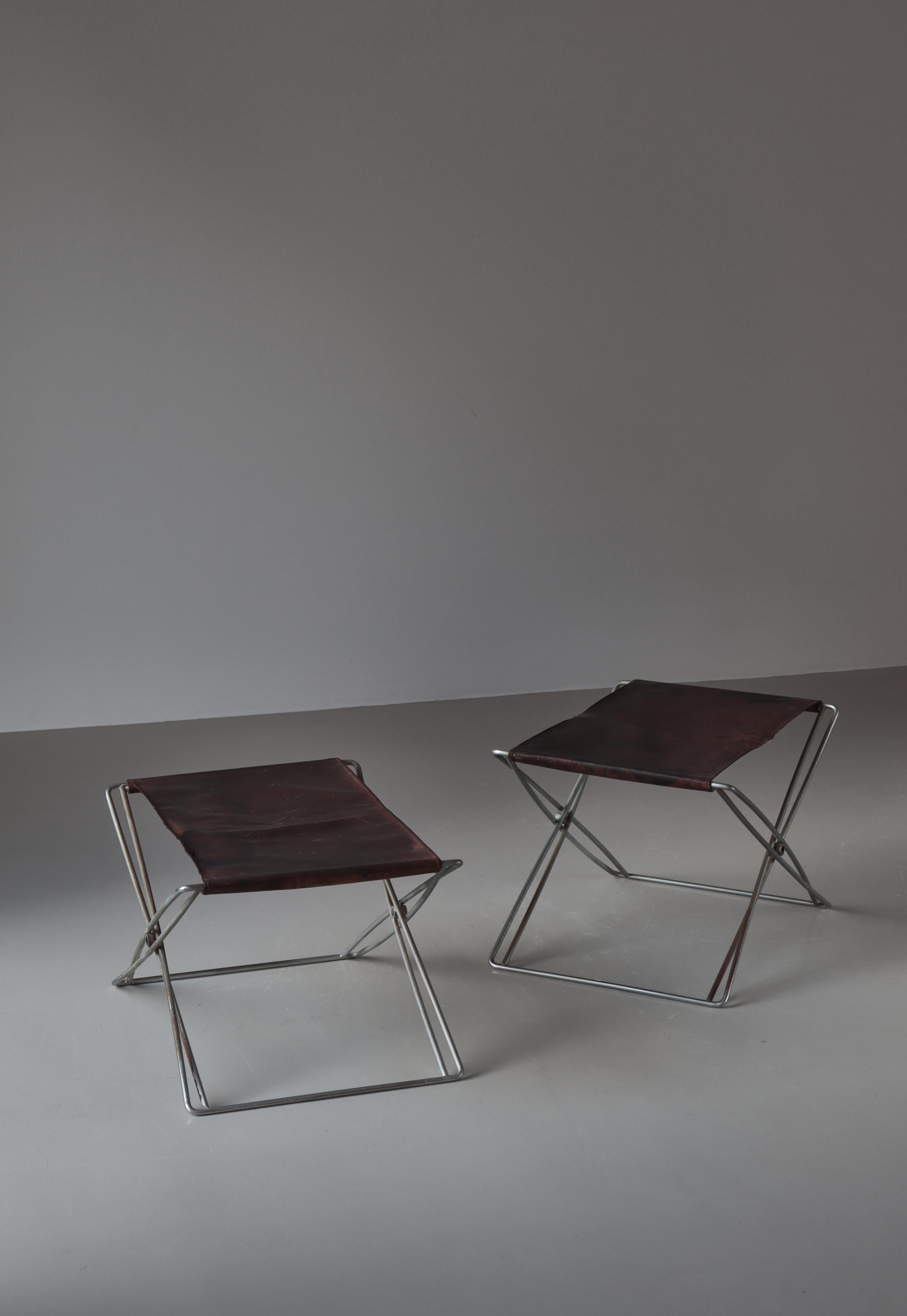 Coppia di sgabelli pieghevoli in acciaio patinato. Seduta rivestita in vinile grigio e pelle naturale. Progettato nel 1970. Prodotto da Design Forum nei primi anni Settanta. Lo sgabello pieghevole è uno dei pezzi più conosciuti di Jørgen
