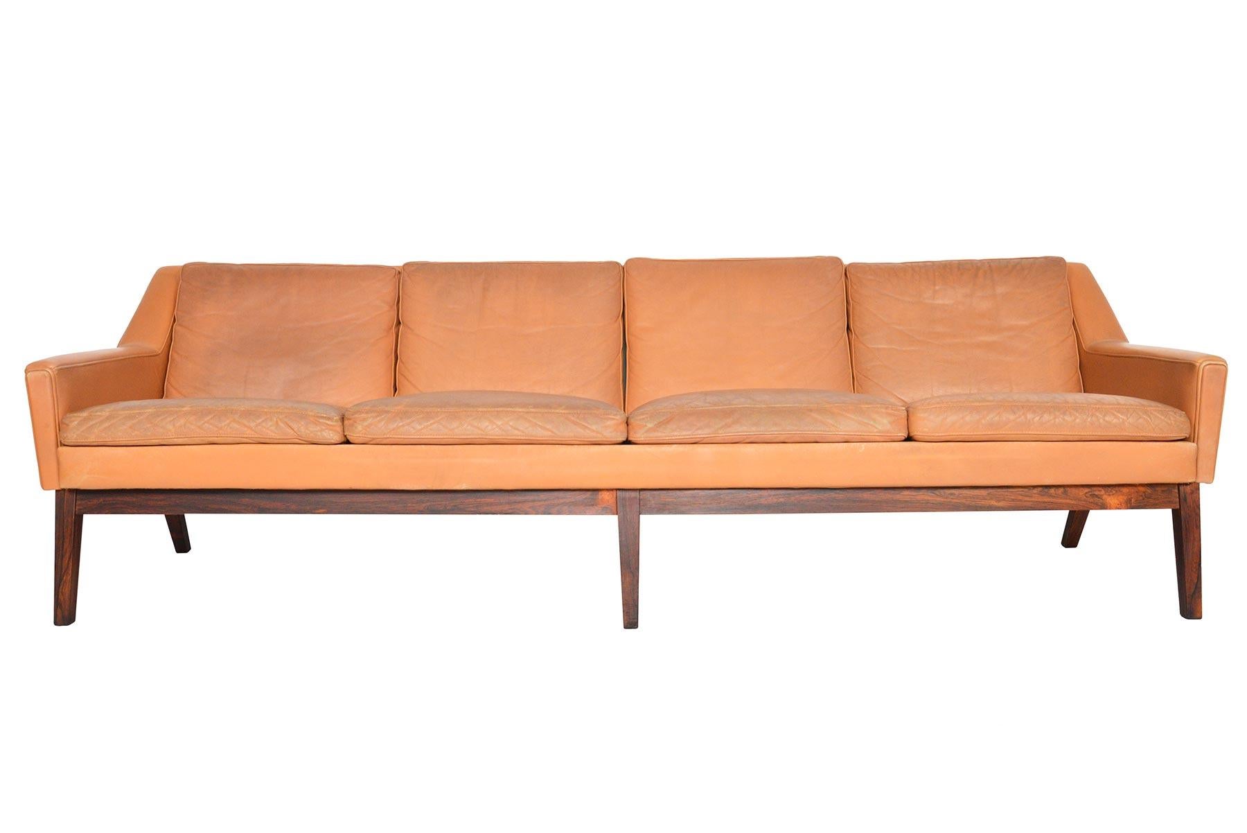 This Danish modern midcentury four seat sofa in patinated sepia leather is a staple of modern decor. Covered in original leather and raised on gorgeous tapered rosewood base, this sofa is upholstered on all sides and can be floated in the centre of