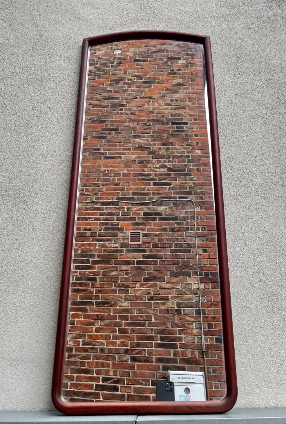A rare full-figure wall hung mirror with solid organically rounded of and hand sanded teak profiles that has been assembled without the use of metal. It was probably designed by Johannes Andersen in Denmark during the early 1960s. Manufactured by E.