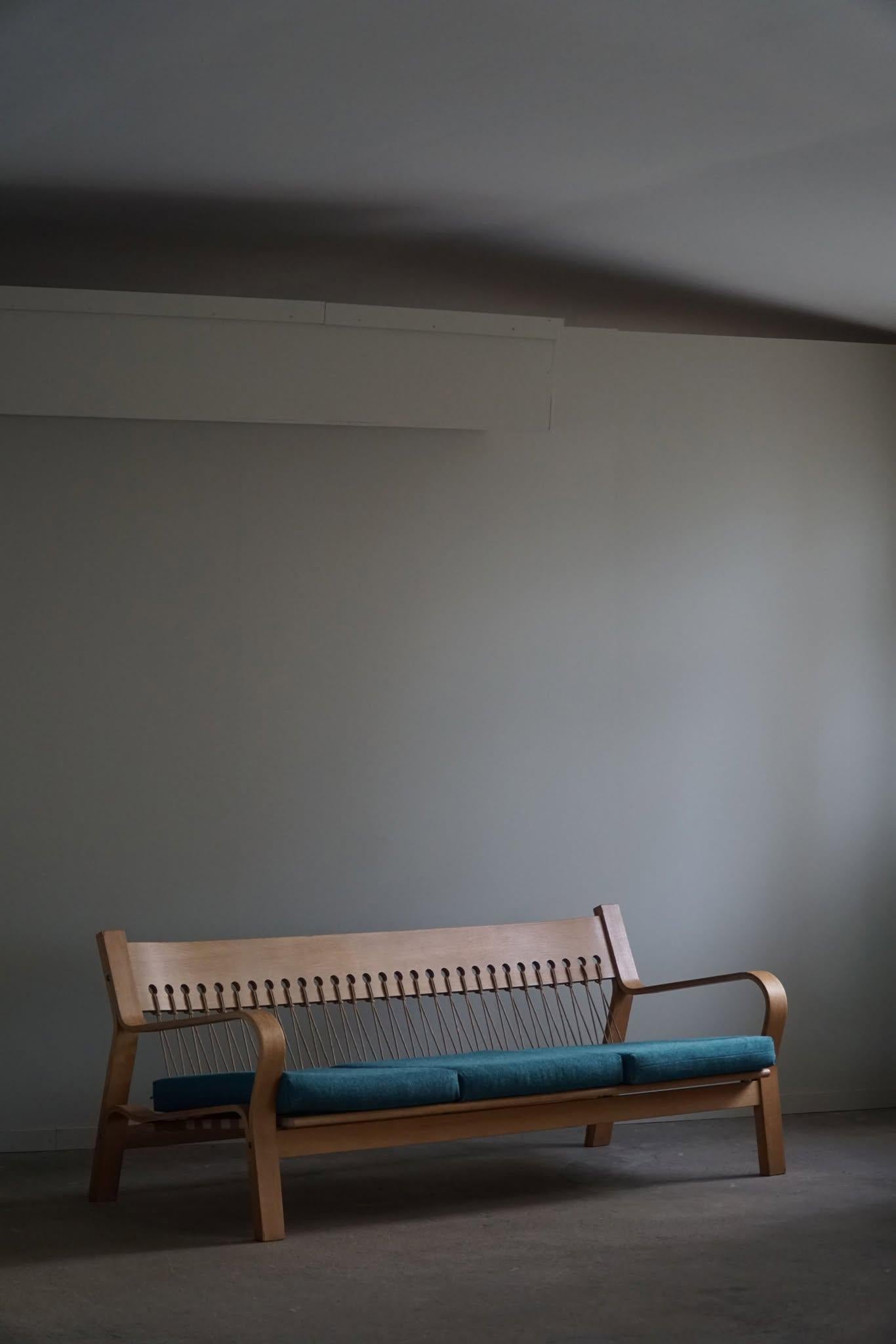 Este sofá modelo GE 671, diseñado por Hans J. Wegner para GETAMA en la década de 1960, está fabricado en roble con un respaldo de driza de bandera en la cuerda de papel original. Los cojines están tapizados con un acolchado de lana. El diseño limpio