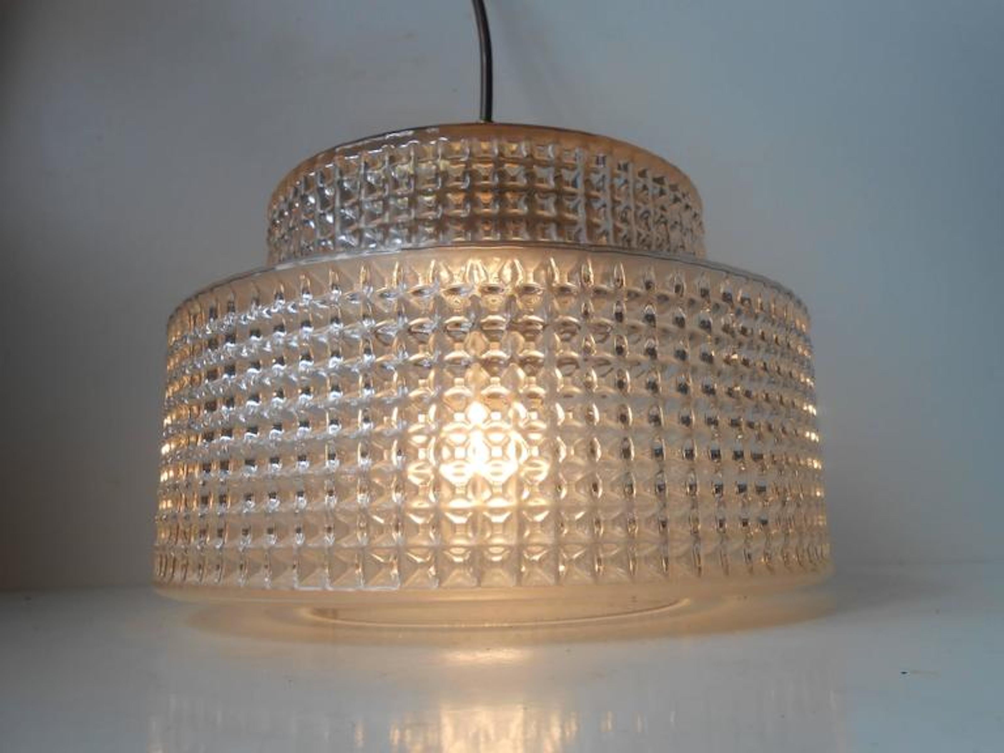 This pendant light was designed and manufactured by Danish design trio Vitrika in the 1960s. The name Vitrika, or Vi-Tri-Ka means 'The three of us can do it'. The lamp features a geometric - diamond patterned clear glass shade. The socket and tube