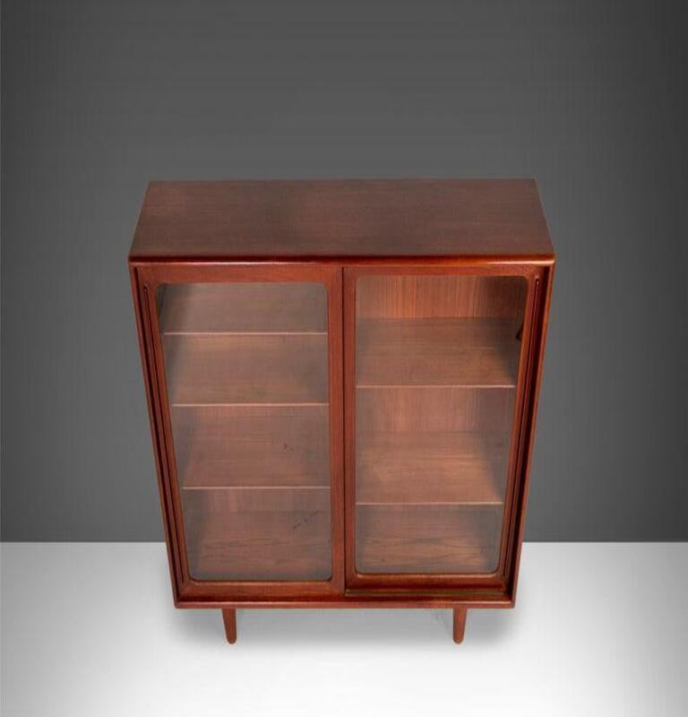 A truly rare and exceptional find designed by Harry Ostergaard, c. 1950s. The cabinet is constructed from teak with large glass sliding doors with long contoured teak pull. The legs have a unique taper adding visual interest. The interior of the