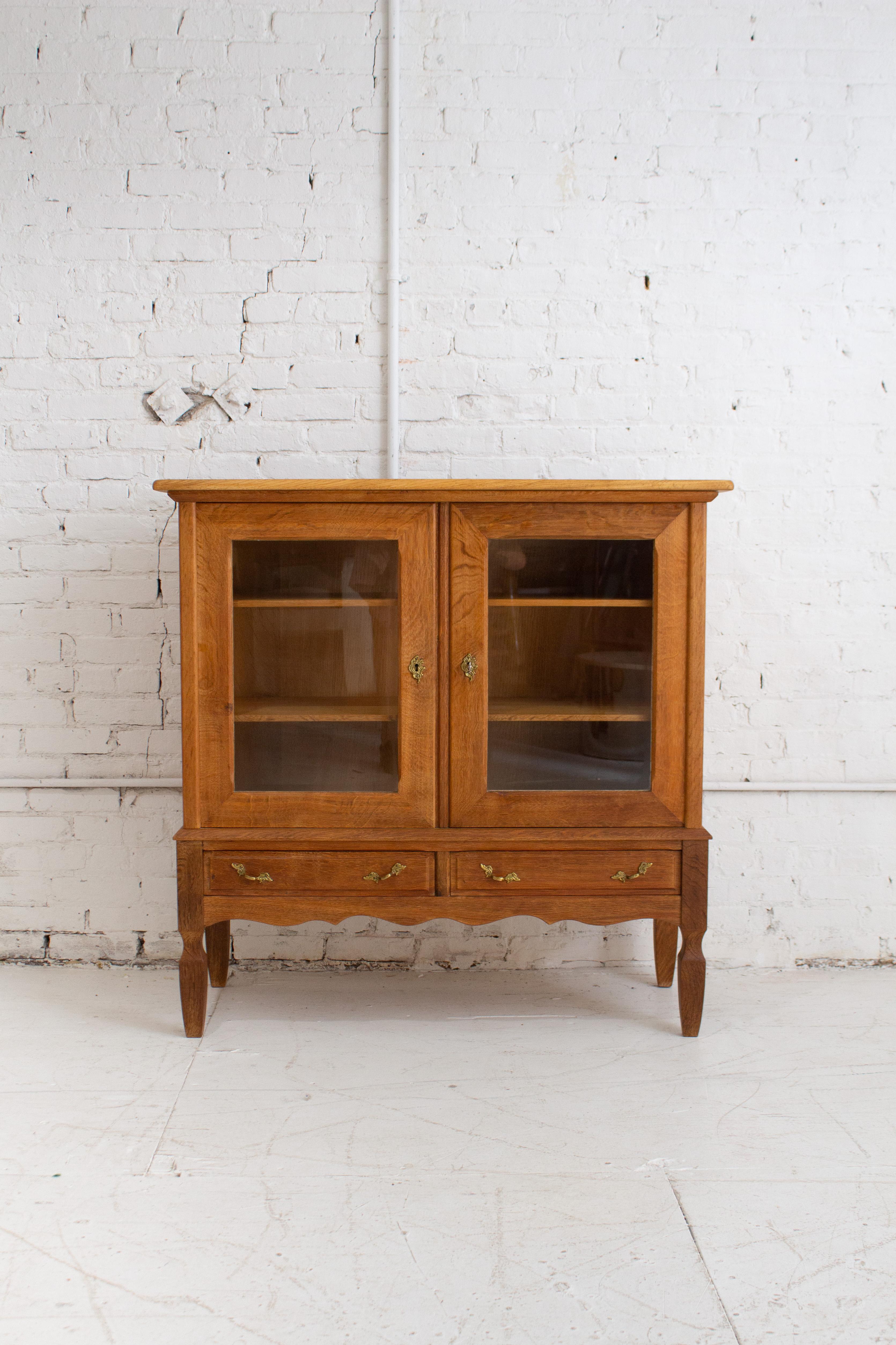 A Danish modern glass front cabinet attributed to Henning Kjaernulf. Blonde oak wood with two lower drawers and two inner shelves. Key included.