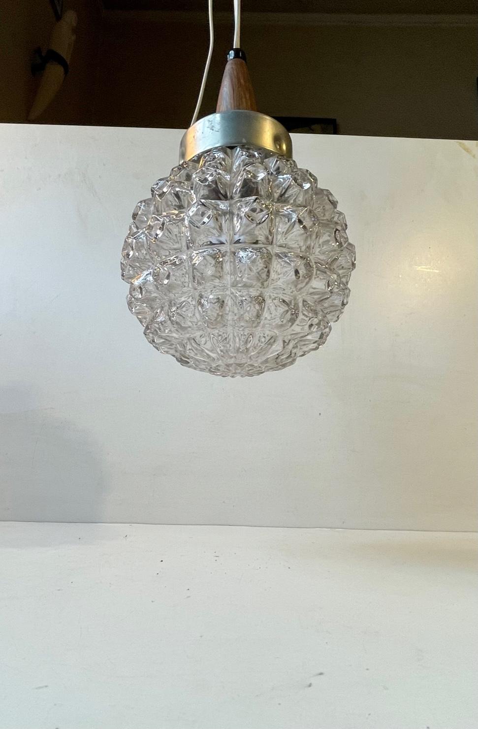 This pendant light was designed and manufactured by Danish design trio Vitrika in the 1960s. The name Vitrika, or Vi-Tri-Ka means 'The three of us can do it'. The lamp features a pineapple - patterned clear glass shade and a rosewood top. It will be