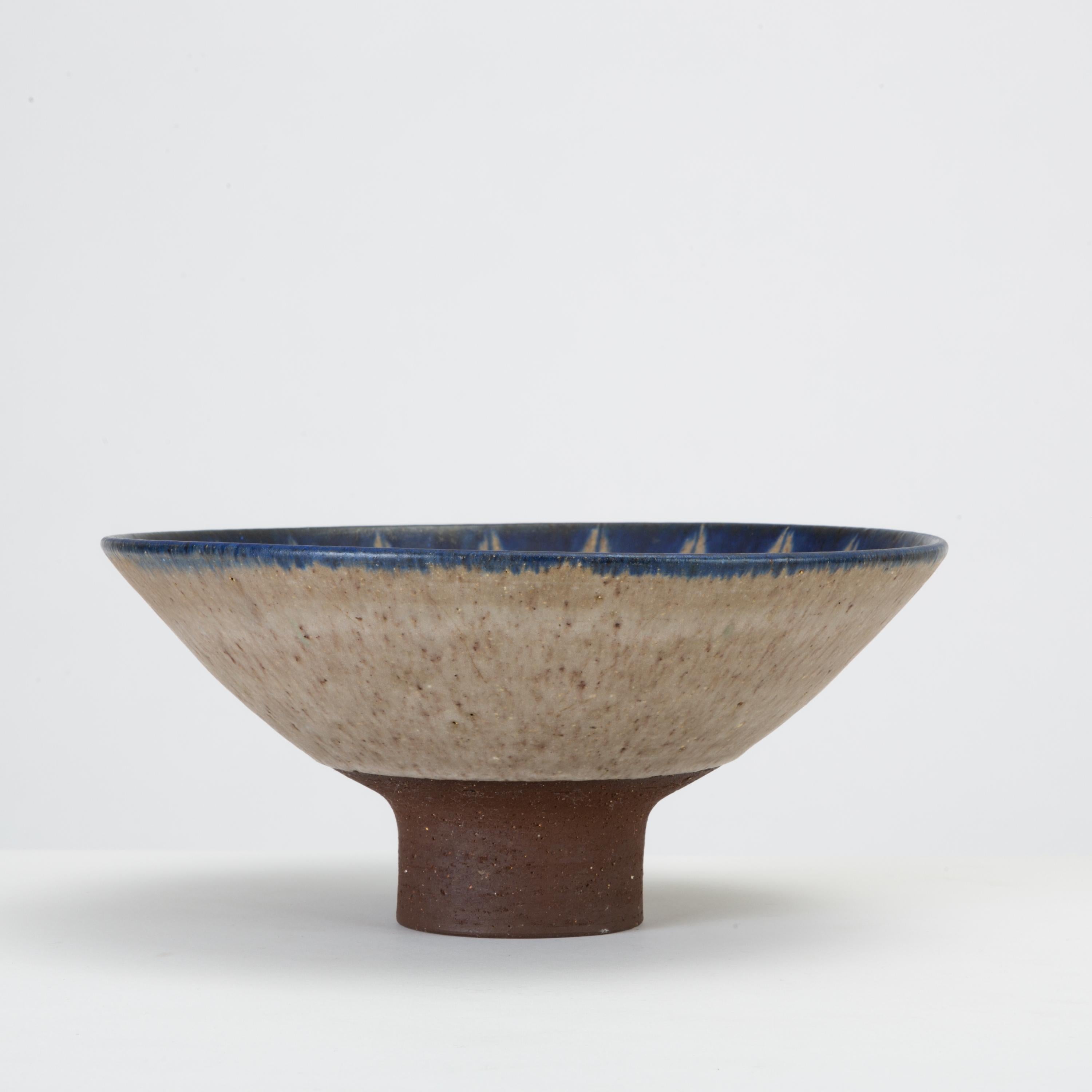 A small, footed stoneware bowl by Danish ceramicist Thomas Toft. The bowl is glazed in a tradition blue and white palate, with a leaf- or flame-like pattern decorating the interior. The dimensional glaze terminates slightly above the foot, leaving