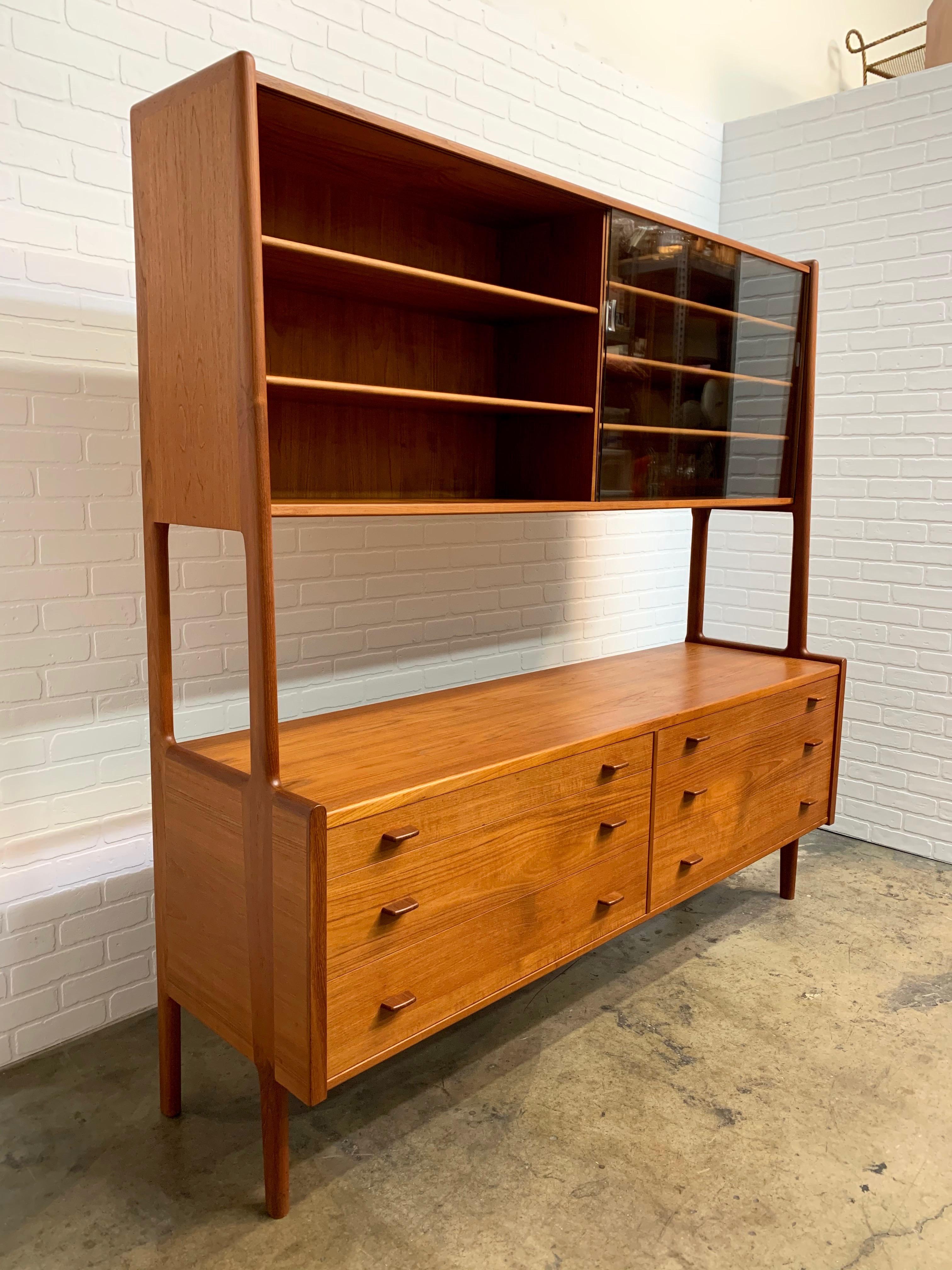 Vintage Danish modern two-tier room divider by Hans Wegner features original teak finish with carved wooden handles. Midcentury sideboard combines glass door display with graduated drawers for concealed storage. Finished on the back.