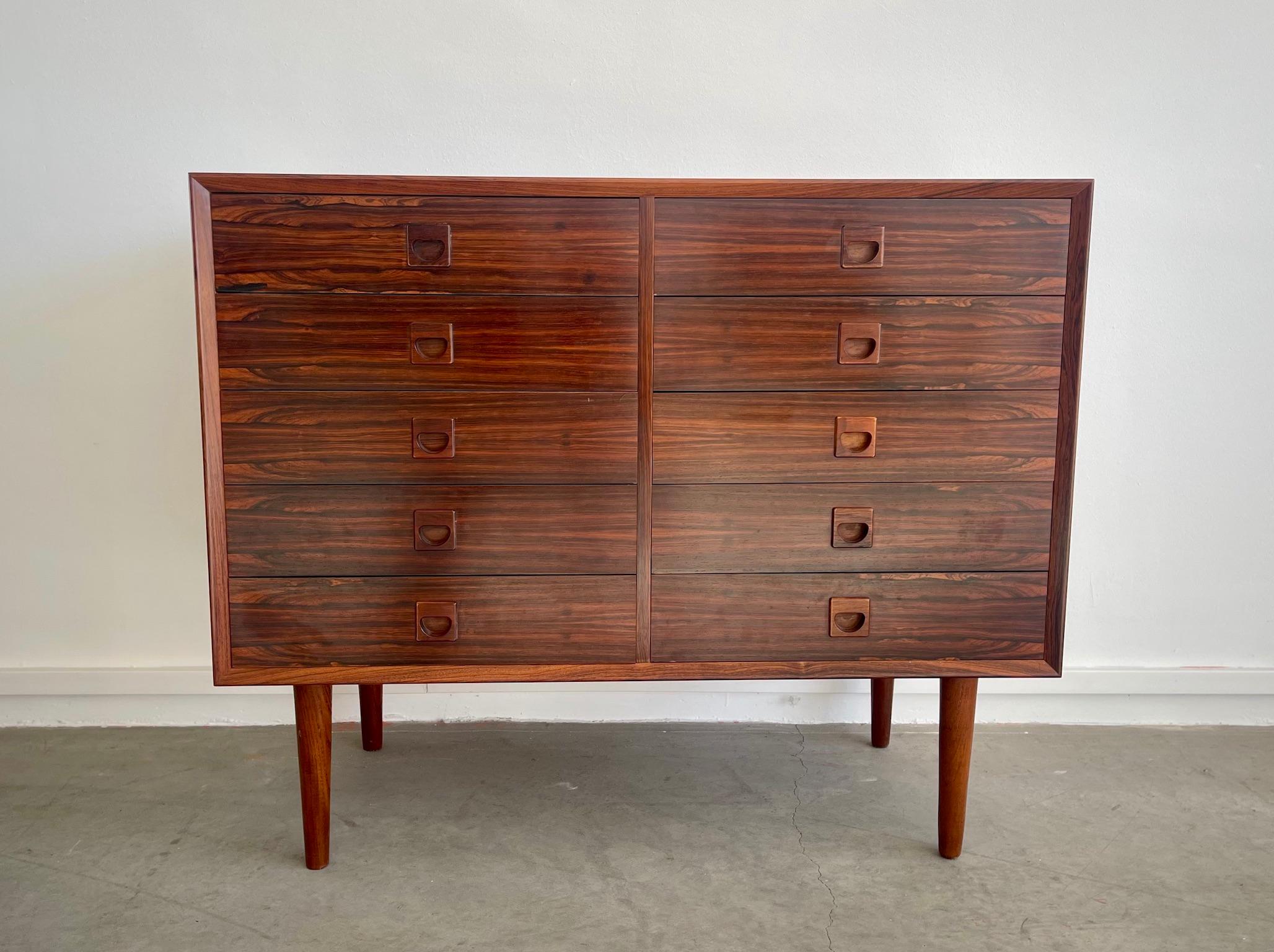 Cassettiera impiallacciata in legno duro marrone scuro con sfumature rossastre, successivamente dotata di gambe in teak. Ogni cassetto è dotato di un'elegante maniglia realizzata con lo stesso legno. Segni di usura dovuti all'età, alcuni graffi