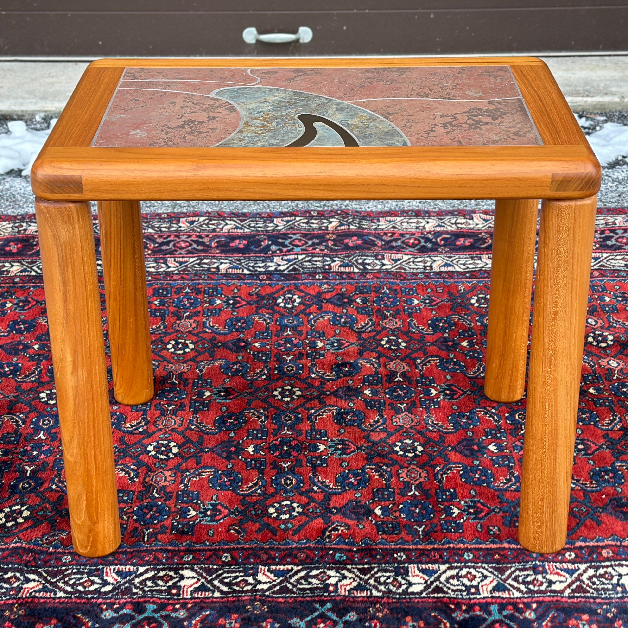 Danish modern side or end table designed by Tue Poulsen for Haslev Denmark features a solid teak frame and cylindrical legs with an intricate handcrafted top in ceramic tile with brass accent. Signed on underside. The legs are threaded and will be