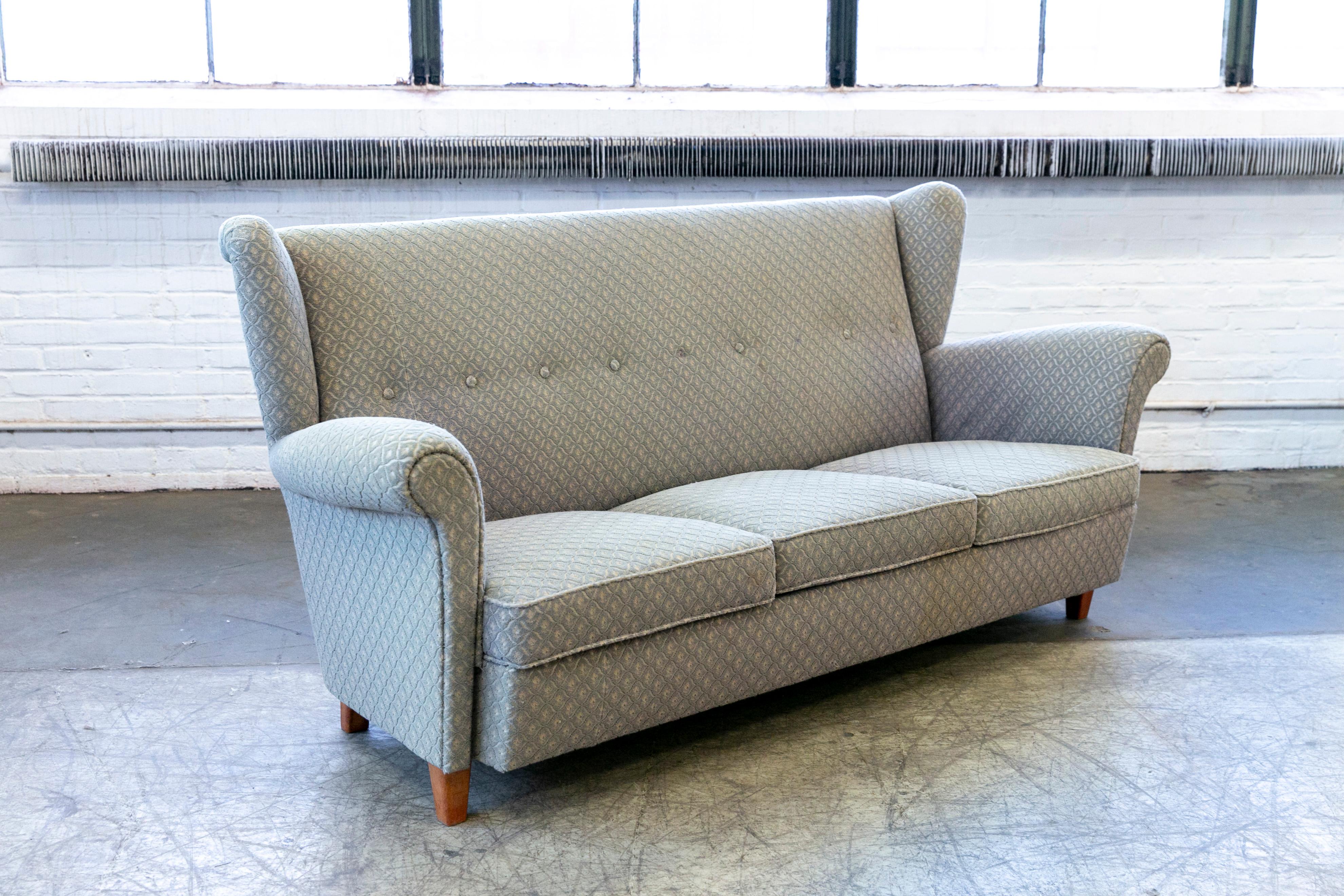 Very charming high back or wingback 1950s sofa from Denmark. The sofa is very reminiscent of Fritz Hansen's model 8112 loveseat but in this case somewhat larger and with a loose seat cushion covered. The piece is unmarked and we are unsure of who