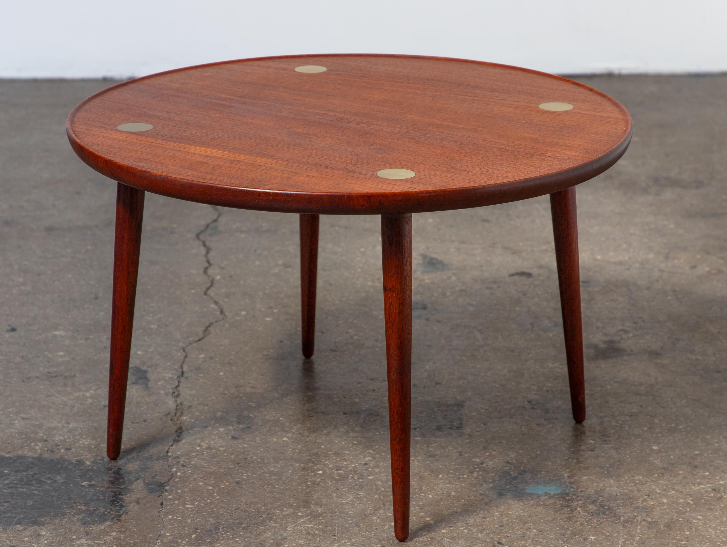 Table de cocktail élégante, conçue et fabriquée par le maître ébéniste danois Jacob Kjær. Fabriquée en teck massif, la table présente un rebord courbé raffiné et des pointes rondes en laiton sur le plateau. Conçue à l'origine en 1939 et produite