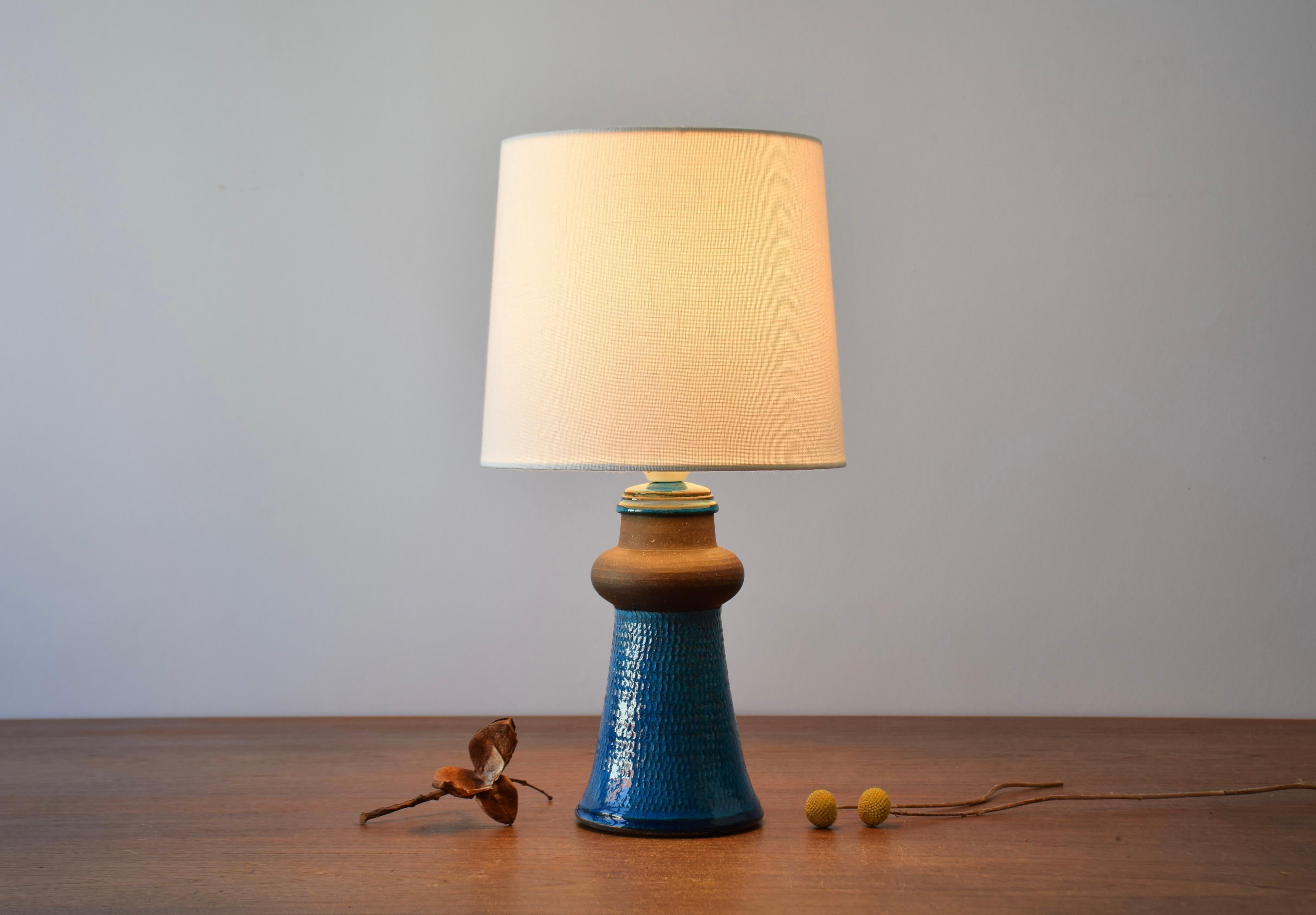 Small midcentury Danish table lamp by Nils Kähler for the ceramic workshop Kähler (HAK).
Made circa 1960s.

It is decorated with a turquoise blue glaze on a structured surface. Part of the neck is left unglazed and shows the dark brown smooth
