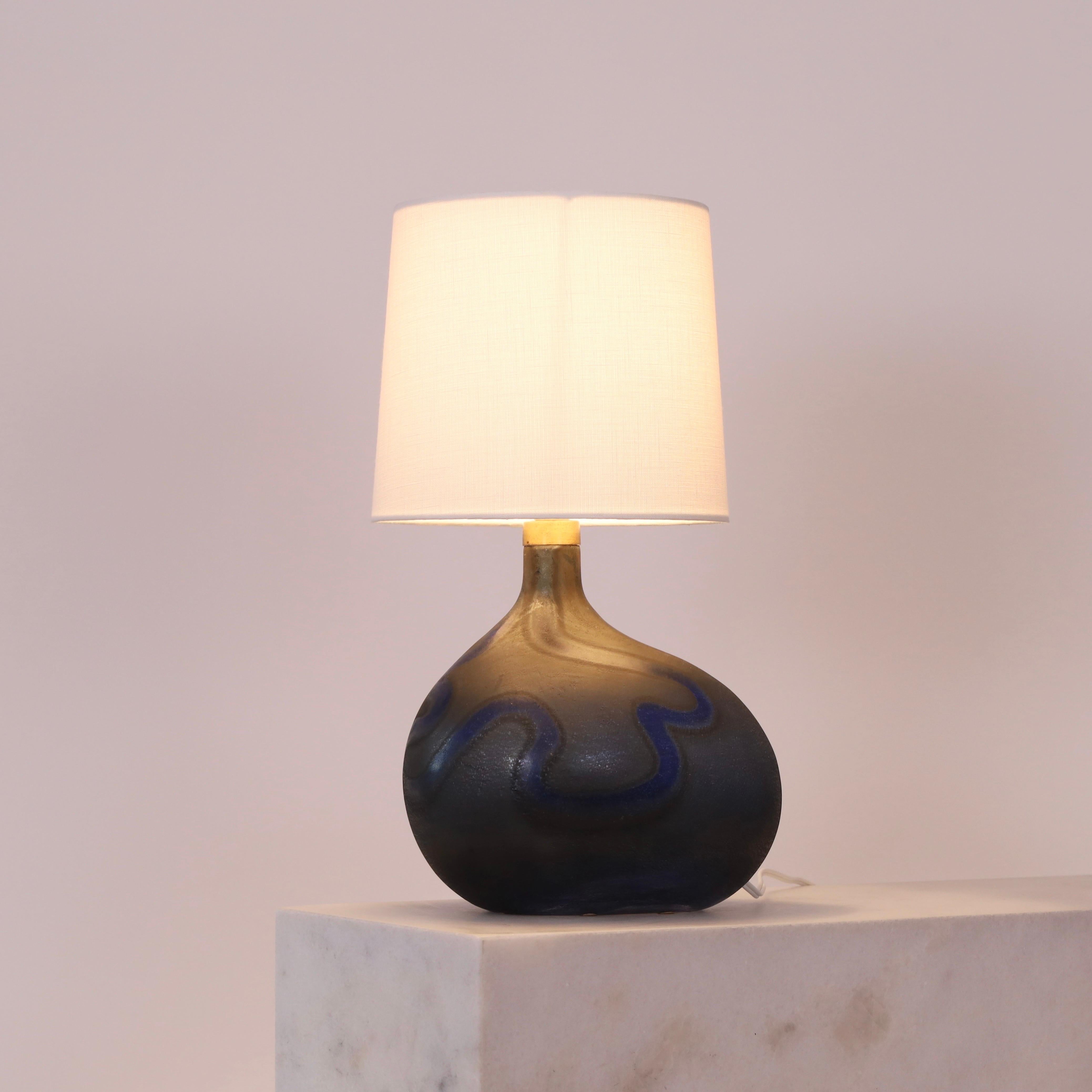 Lampe de bureau en verre de forme organique conçue par Michael Bang en 1972 pour Holmegaard, Danemark. Irrésistible à l'œil.

* Lampe de table en verre organique à motifs bleus avec un abat-jour en tissu blanc.
* Designer : Michael Bang 
* Style :