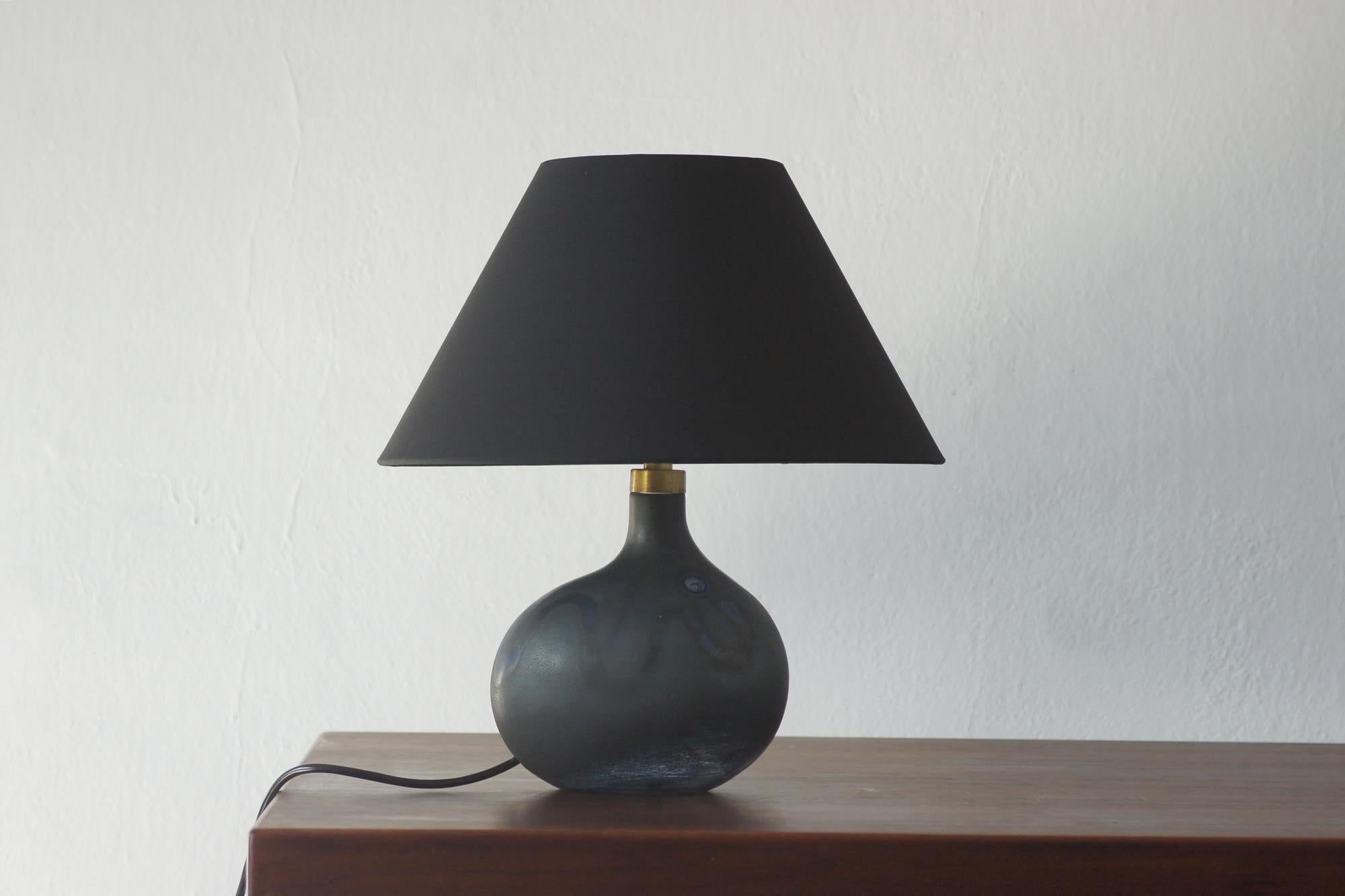 Eine außergewöhnlich elegante und unverwechselbare Glastischlampe, die in den 1970er Jahren von Michael Bang für Holmegaard in Dänemark entworfen wurde.

Der Leuchtenfuß hat eine organische, asymmetrische Form, die typisch für das skandinavische