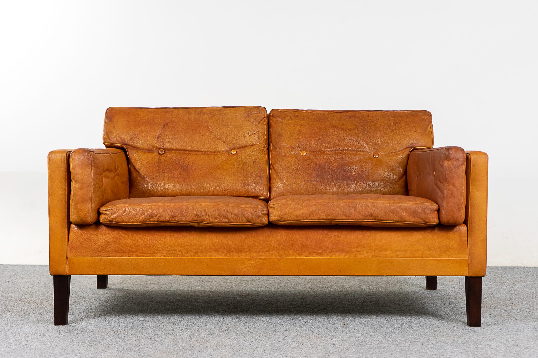 Leather Danish loveseat, circa 1960's. Well loved original tobacco leather upholstery and solid wood legs. Some wear and tear, as shown in photos. 

Please inquire for remote and international shipping rates.