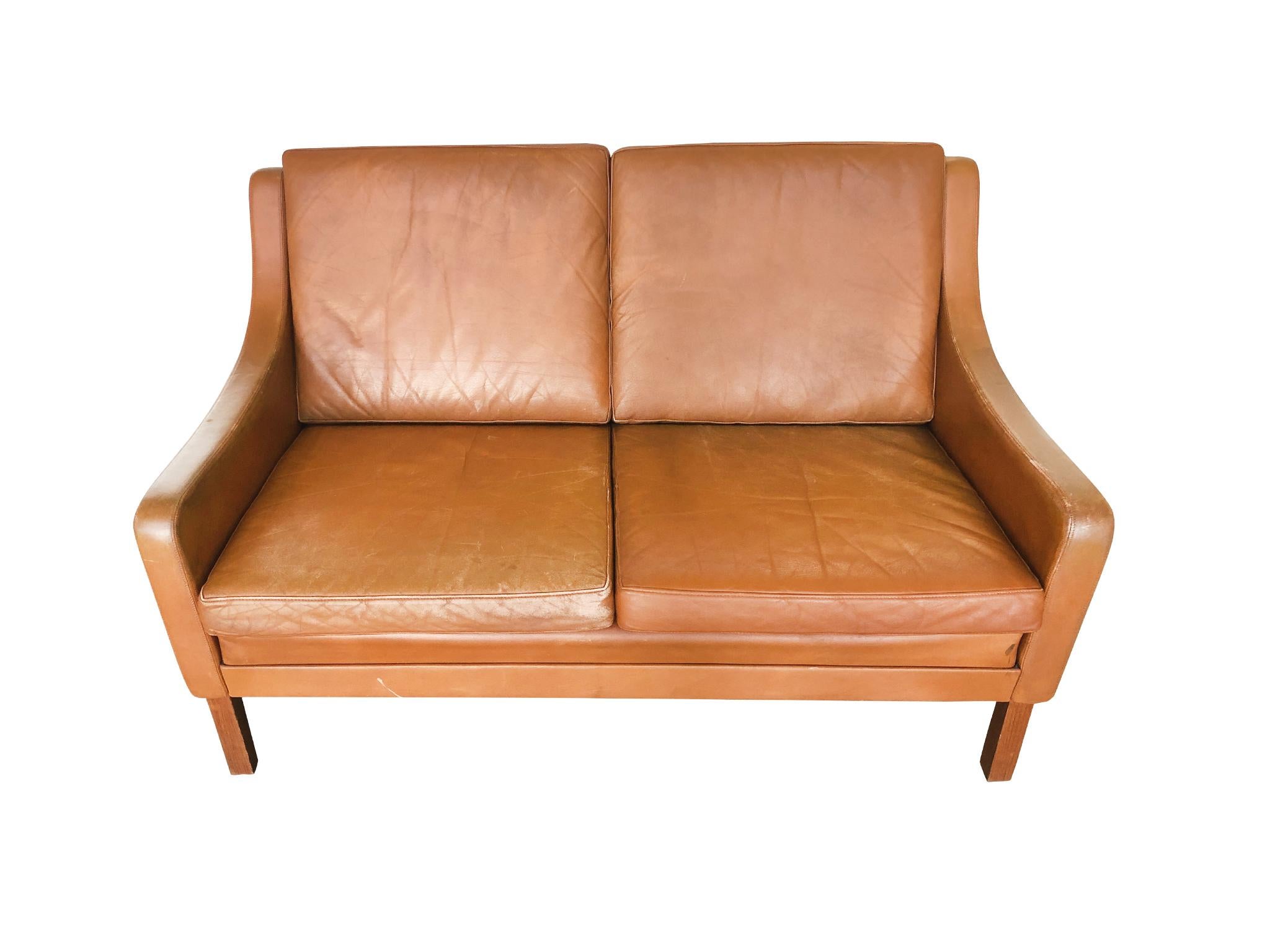 An elegant leather settee designed in the manner of Børge Mogensen. Manufactured 1970s-1980s. Like Mogensen's creations, this settee is designed with Classic smooth lines and soft, rounded edges. The upholstery is a well-aged leather in