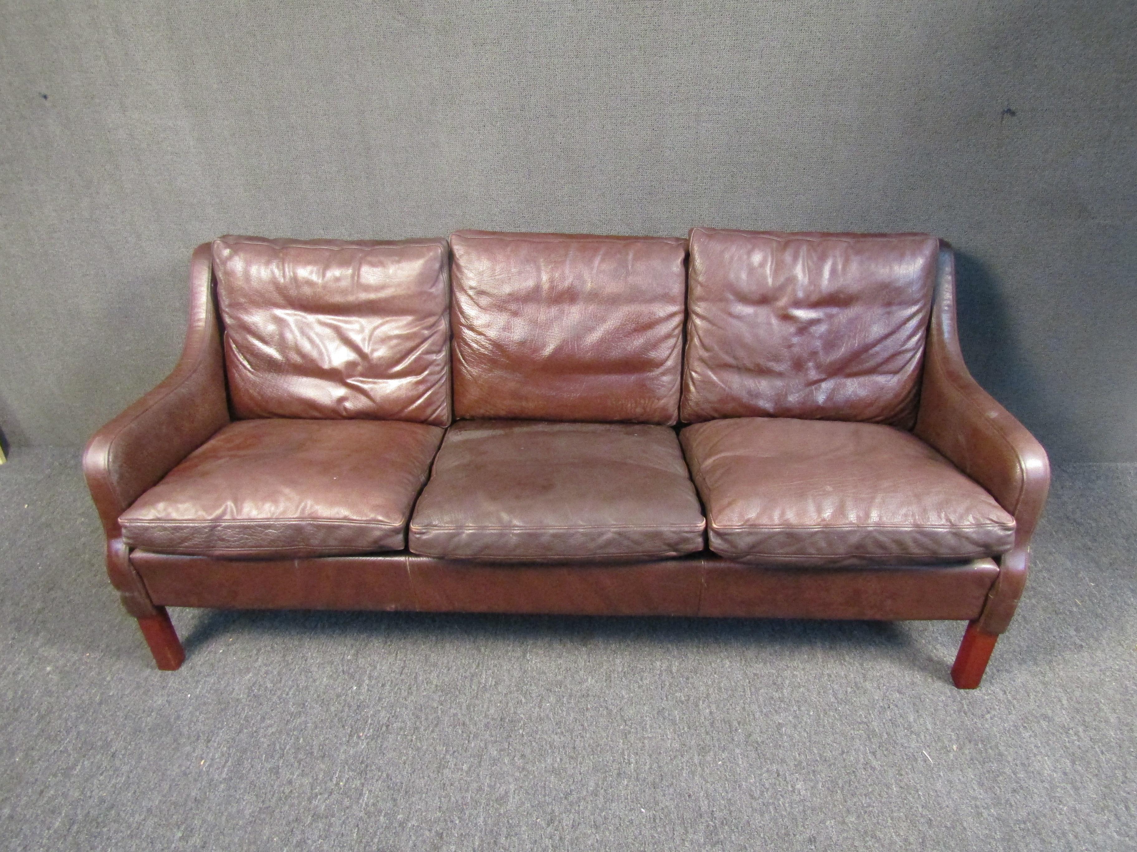 Mid-Century Modern danish style burgundy leather sofa. Featuring sloped arm rests and rich wood grain legs.

Please confirm item location (NY or NJ).