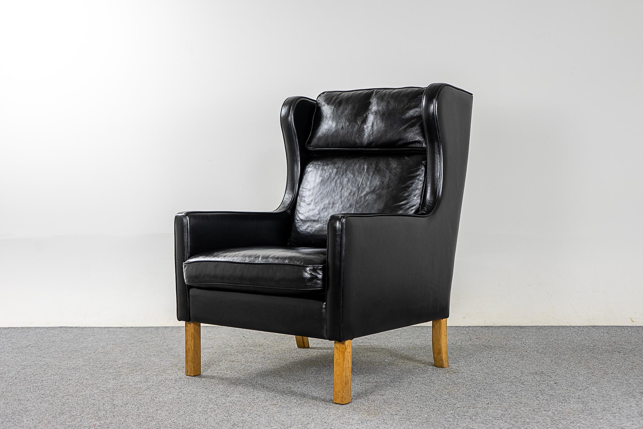 Leather Danish modern pitch black wingback lounge chair, circa 1960's. Classic high back provides support for your neck, sit back and relax! Contrasting wood legs, a nice touch.

Please inquire for international shipping rates.