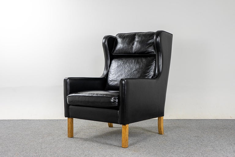 Leather Danish modern pitch black wingback lounge chair, circa 1960's. Classic high back provides support for your neck, sit back and relax! Contrasting wood legs, a nice touch.
