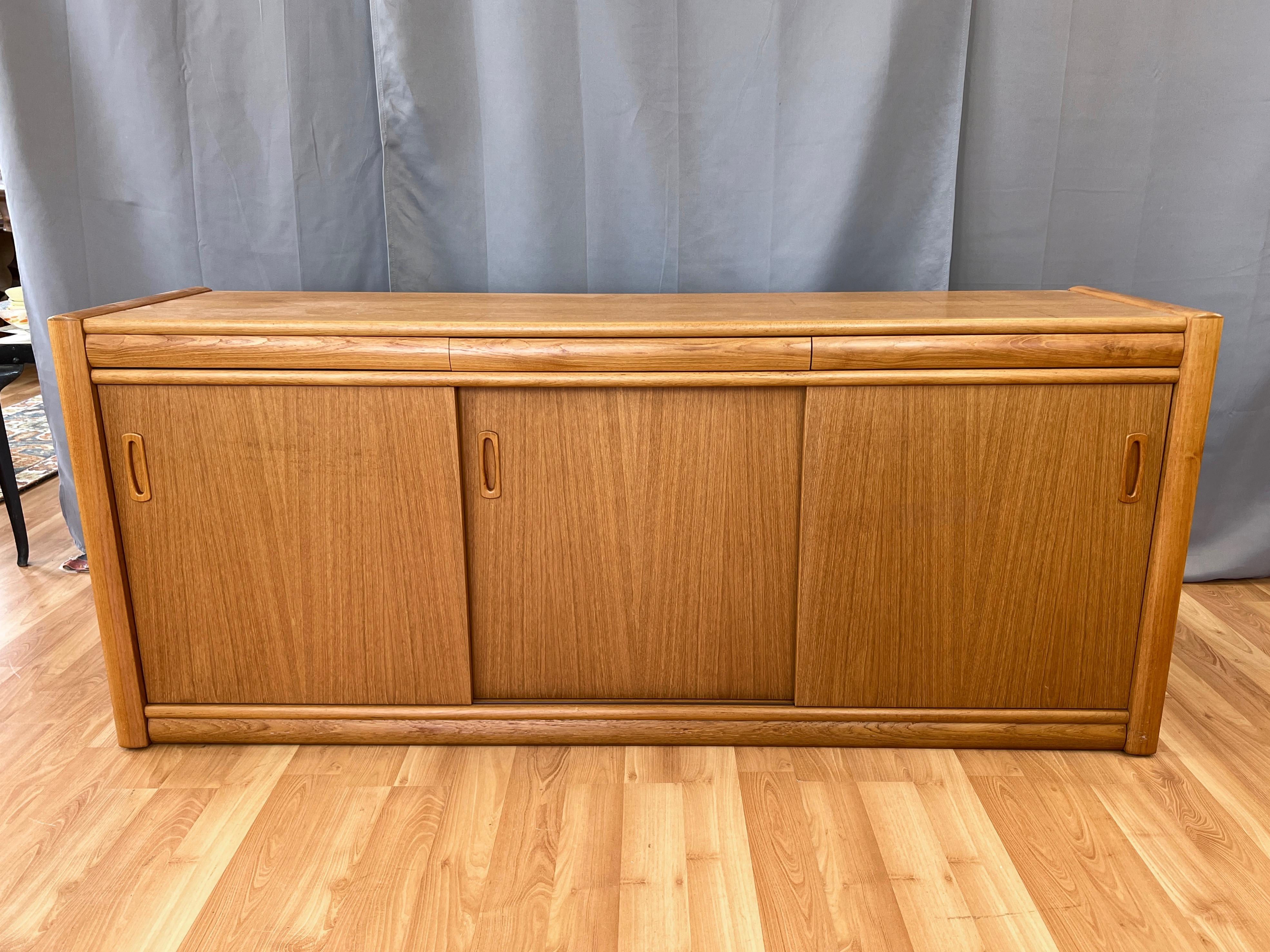 A very handsome 1970s six-foot-wide Danish teak sideboard with three sliding doors and three push-to-open drawers.

Clean Scandinavian modern design in bookmatched teak with nicely rounded edges and abundant storage space within. Features a trio of