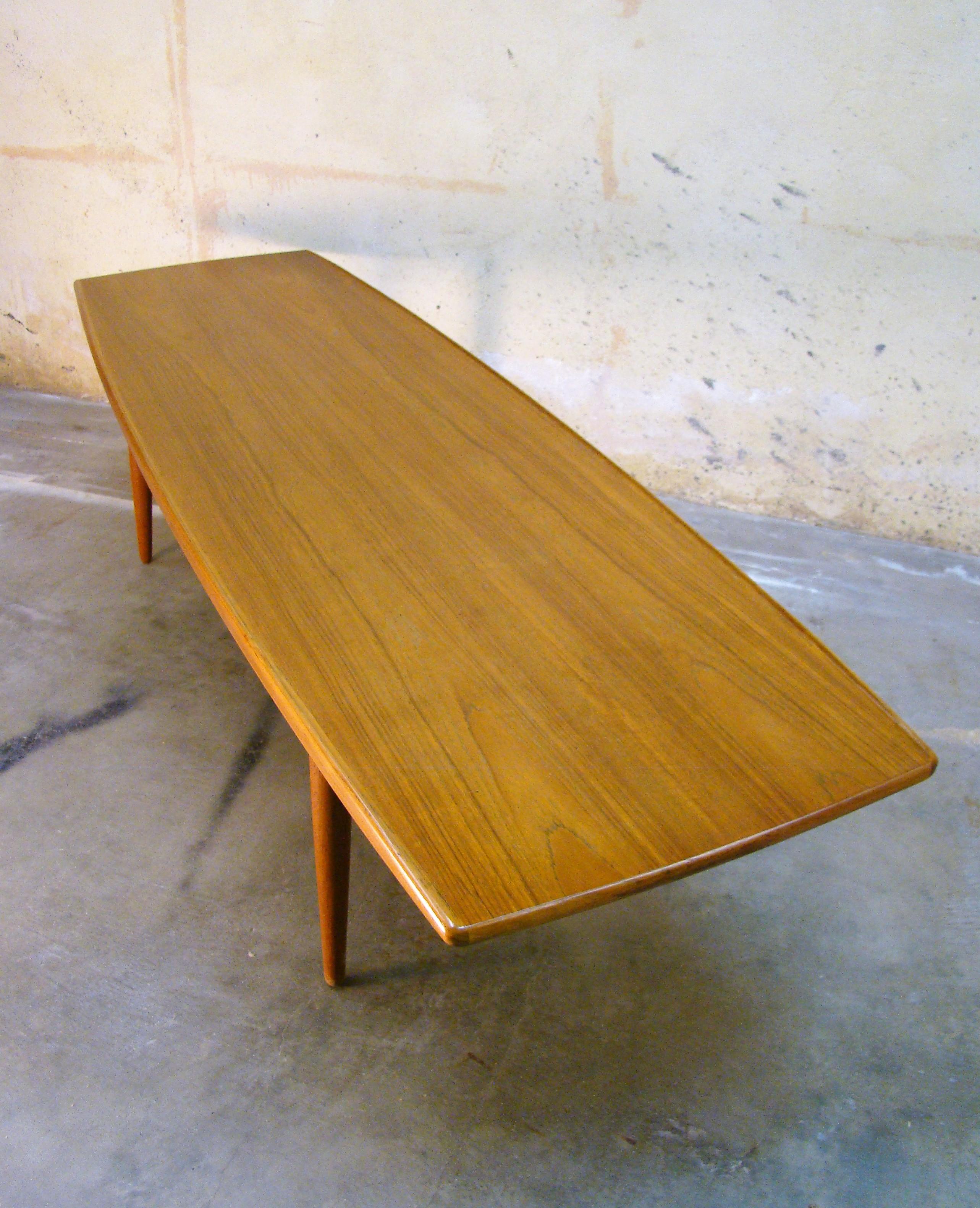 Large, long, lipped edge midcentury Danish modern teak surfboard coffee table marked KT of Denmark, circa 1950s, this stunning table has the size, stance and build quality needed to complete your Mid-Century Modern living room. Four turned, tapered