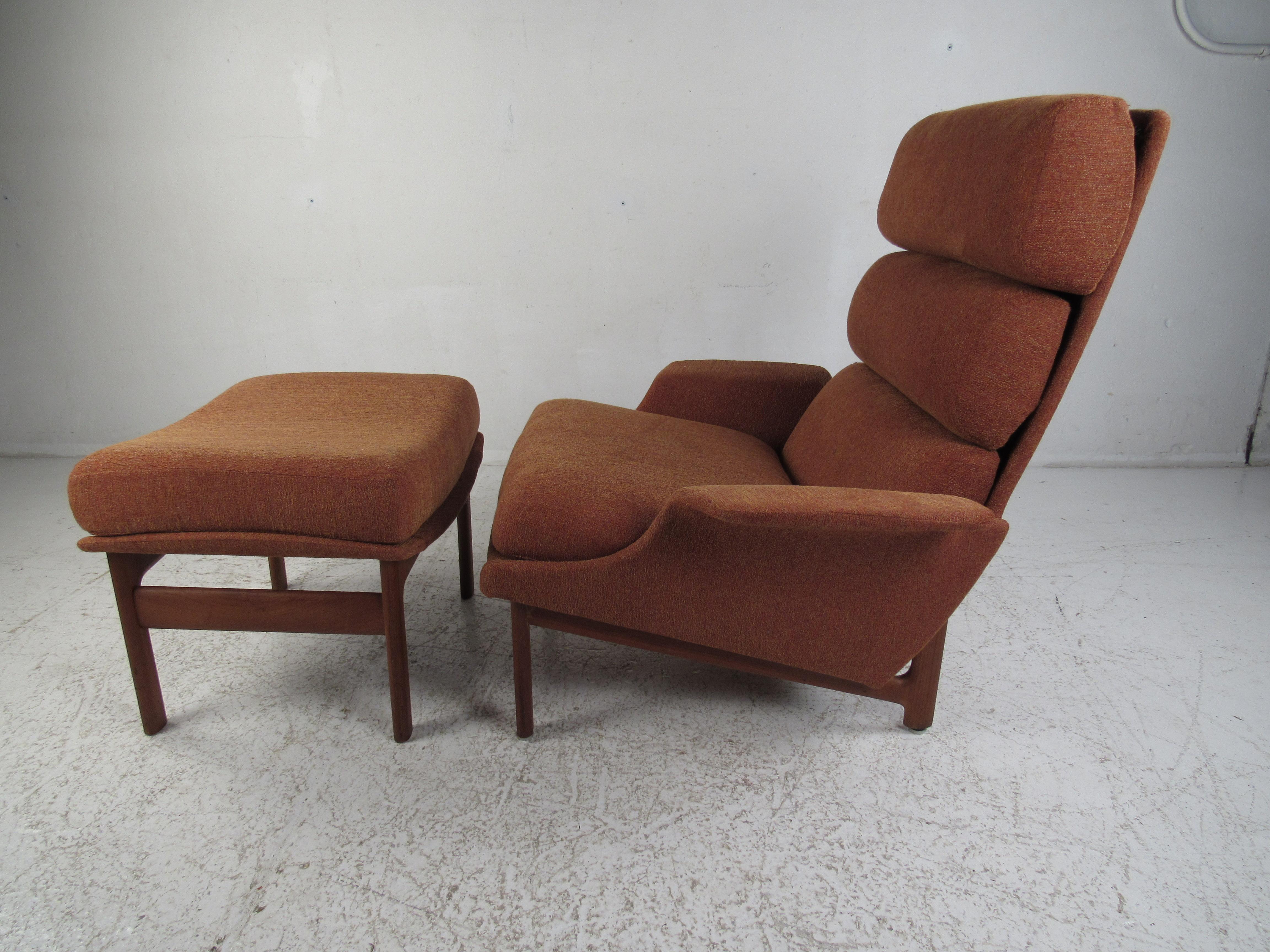 This stunning Mid-Century Modern lounge chair boasts winged arm rests, a high backrest and overstuffed cushions. This rare armchair and matching ottoman sit on a sturdy teak base. The soft orange colored upholstery and angled design ensures maximum