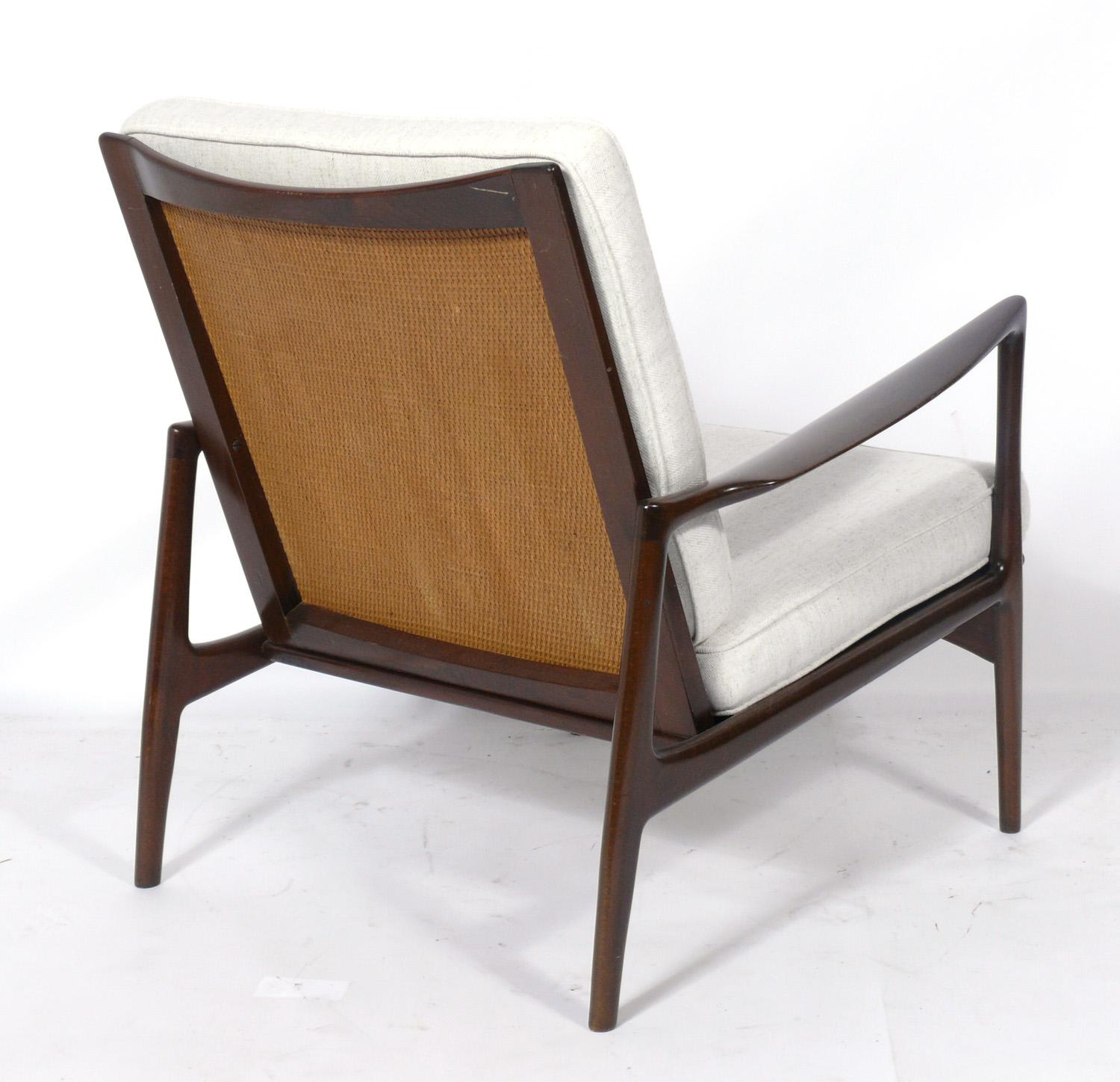 Danish modern caned back lounge chair, designed by Ib Kofod Larsen for Selig, Denmark, circa 1960s. It has been cleaned and Danish oiled. It has recently been reupholstered in a ivory color herringbone upholstery with new foam cushions.