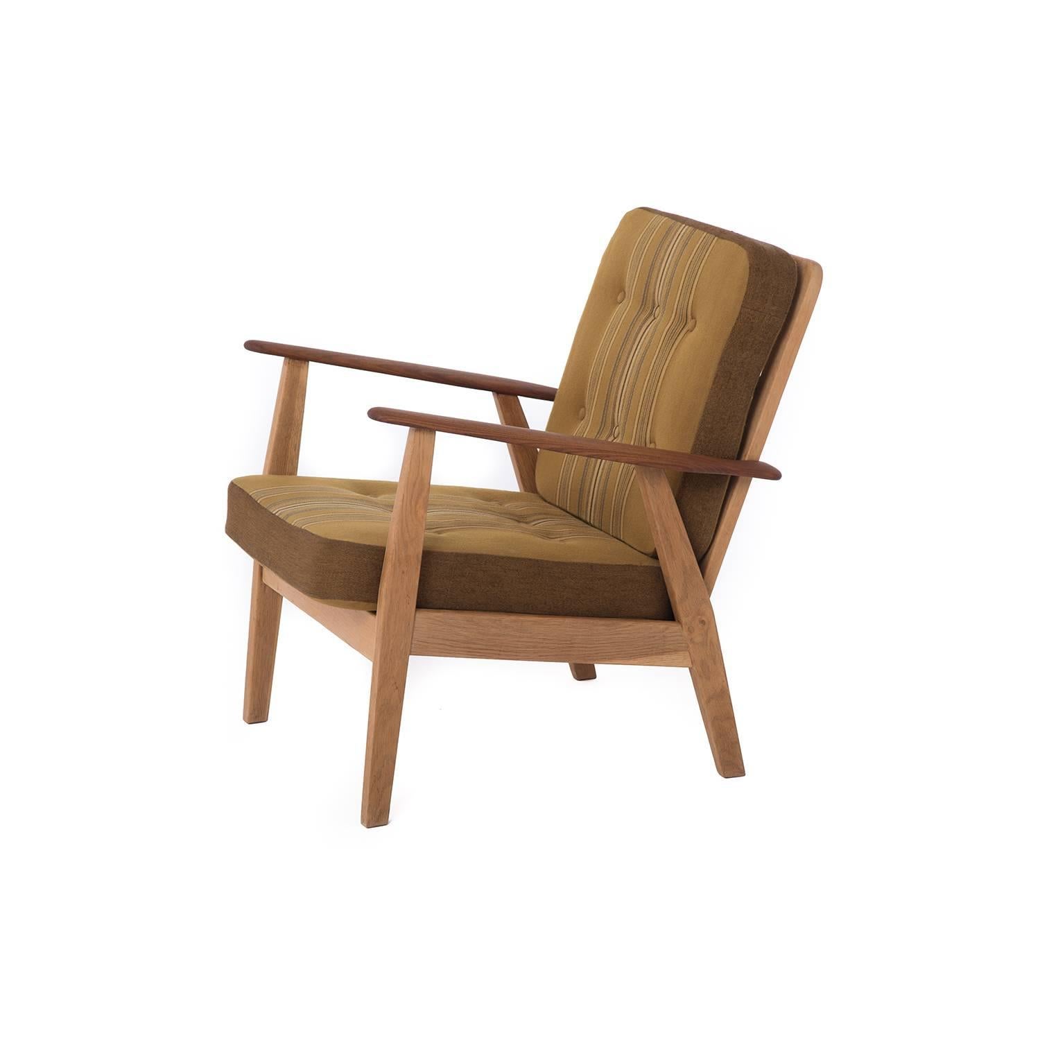 This Danish lounge chair in original vintage upholstery features sculptural teak arms atop a sturdy oak base.