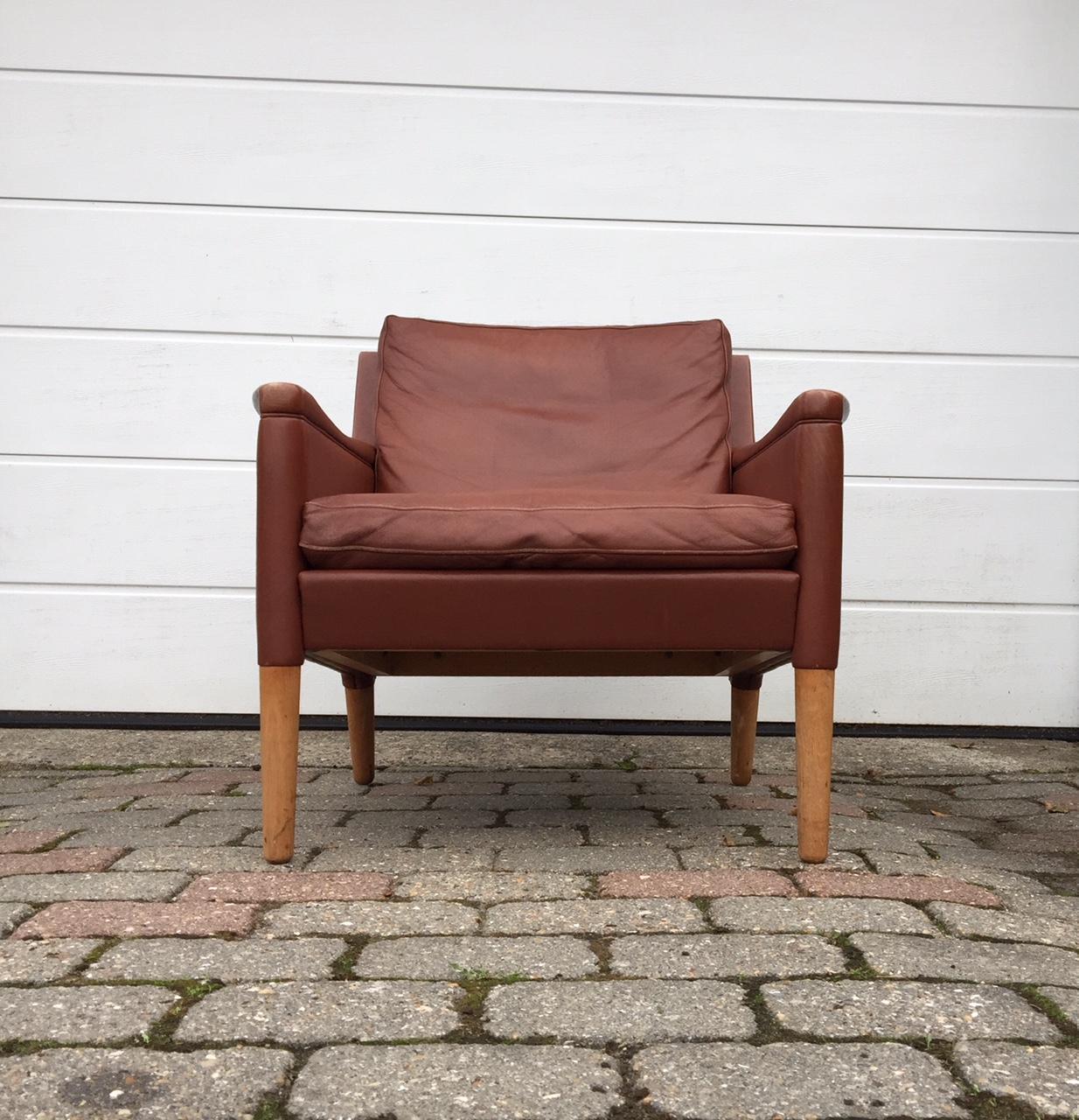 Kurt Ostervig designed tanned leather easy chair with tapered oak legs. It features original upholstery and intricate leather upholstery details around the top part of the legs and to the armrests. It was manufactured by Centrum Møbler in Denmark