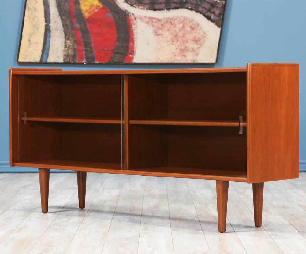 Danish Modern Low Profile Bookcase designed and manufactured in Denmark circa 1960's. Beautifully crafted in a low profile teak wood frame and tapered legs, this Danish design features two compartments with removable shelves and maintains its