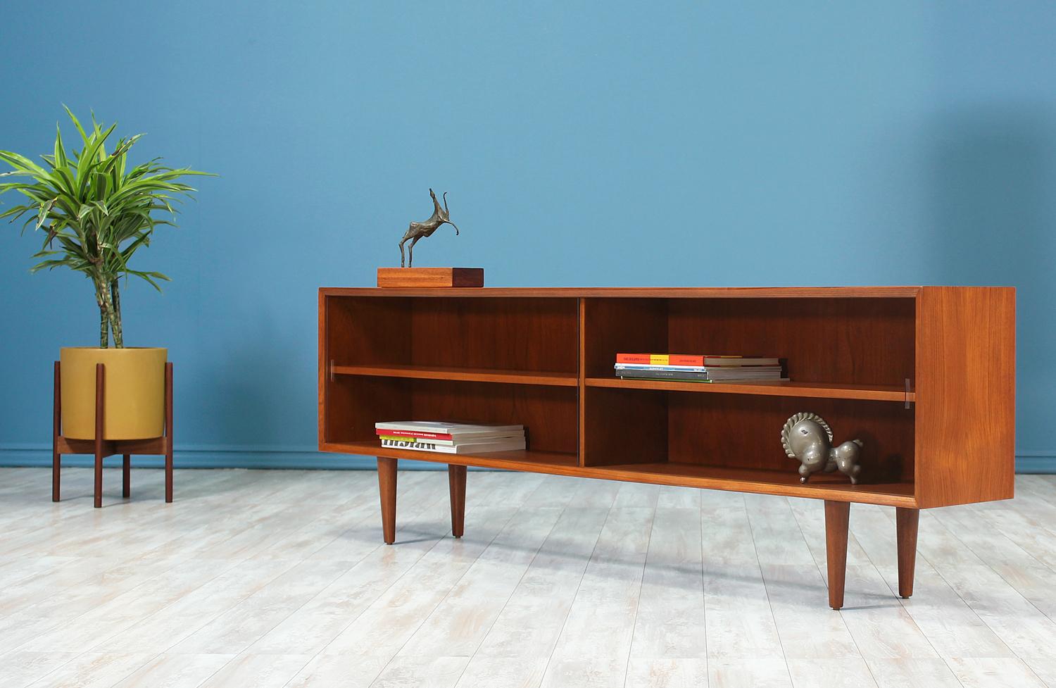 Danish Modern bookcase designed and manufactured in Denmark circa 1960’s. Beautifully crafted in teak wood, this stunning bookcase sits on 8” tapered legs and features two compartments with removable and adjustable wood shelves. The glass doors