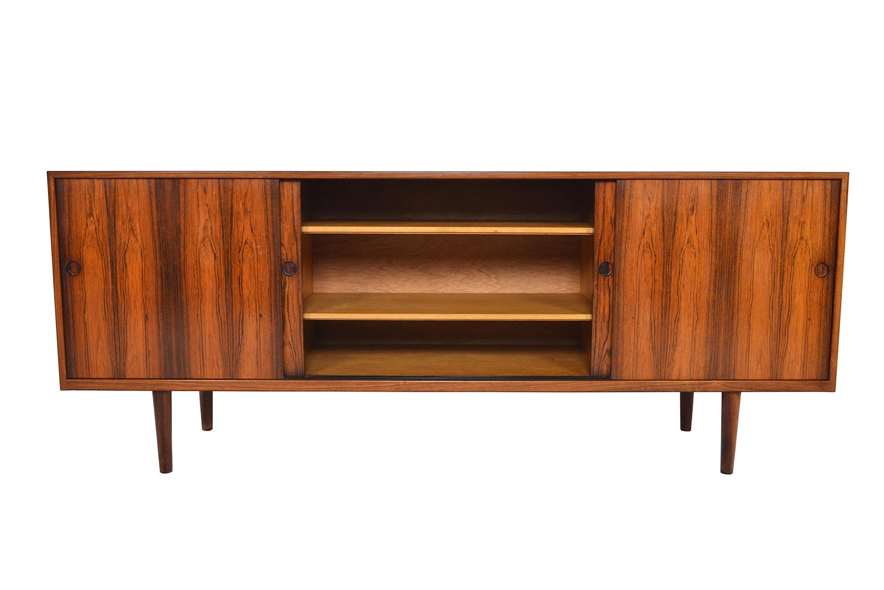 Beautifully simple and effortlessly modern, this Danish modern credenza in rosewood offers exceptional grain patterns on all sides. Four sliding doors with carved pulls open to reveal three bays with adjustable shelving. The left and right bays