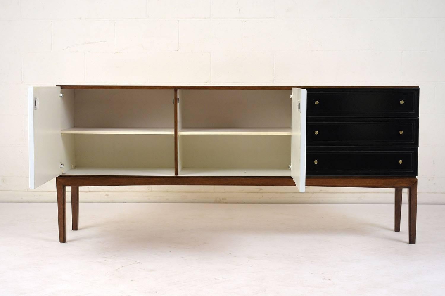 This 1960s Danish Lubke credenza is made of teak wood finished in a rich walnut color with a black and white facade and a lacquered finish. There are three drawers and two cabinet doors with brass knobs. Inside the cabinets there is two sections